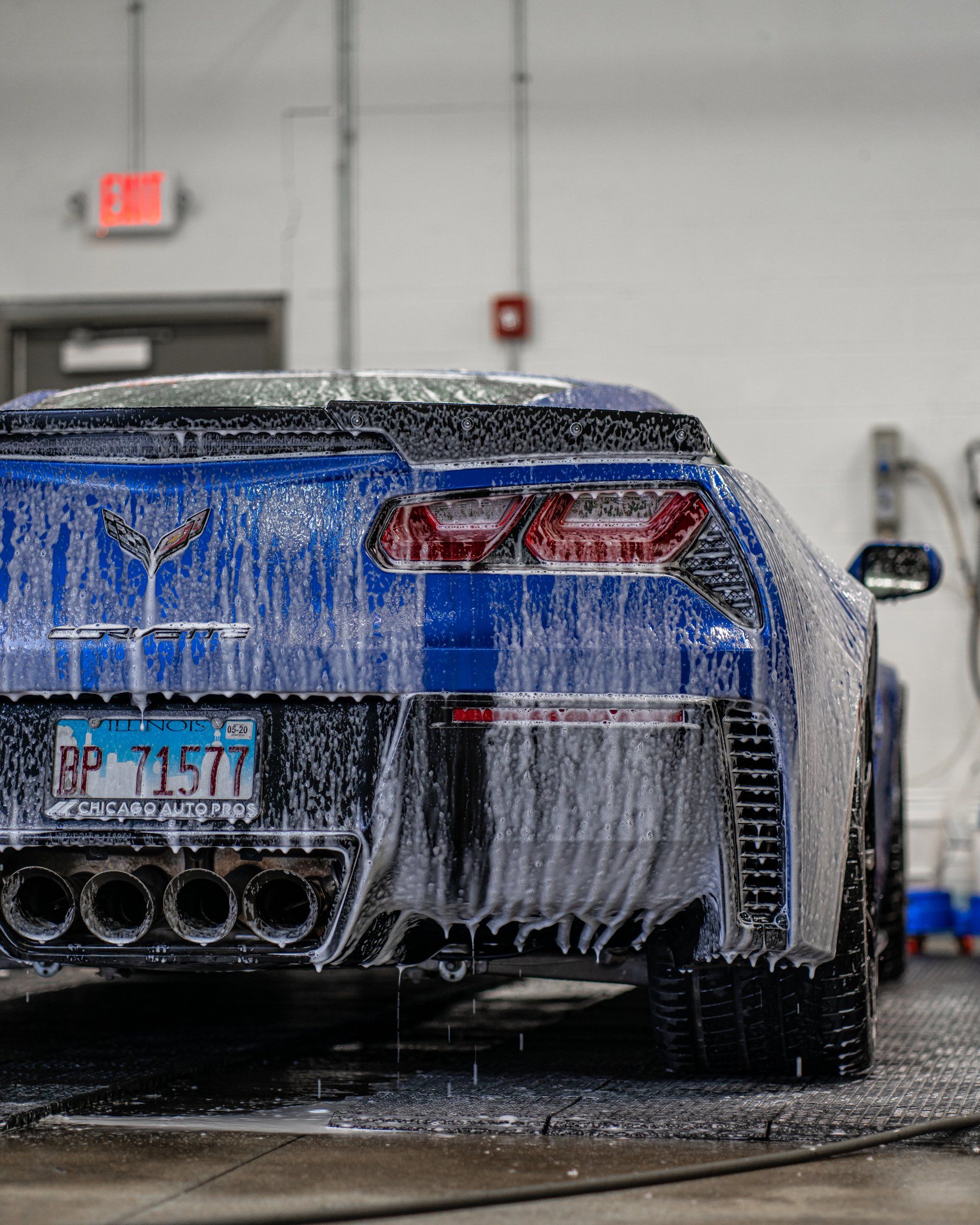A blue sports car is covered in foam in a garage.