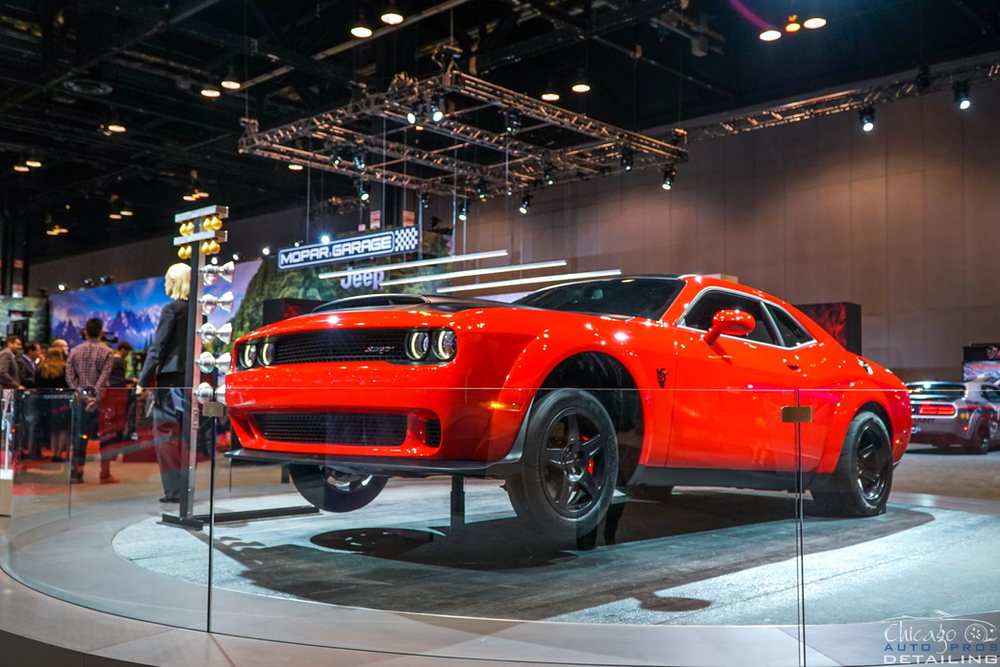 A red dodge challenger demon is on display at a car show.