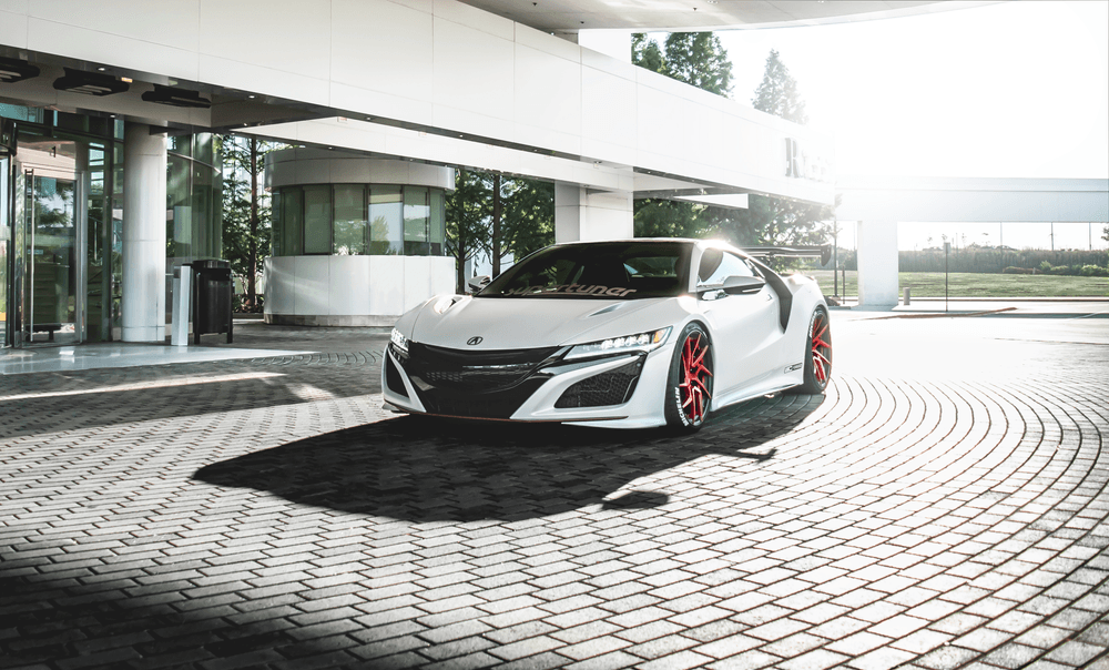 A white sports car is parked on a brick driveway in front of a building.