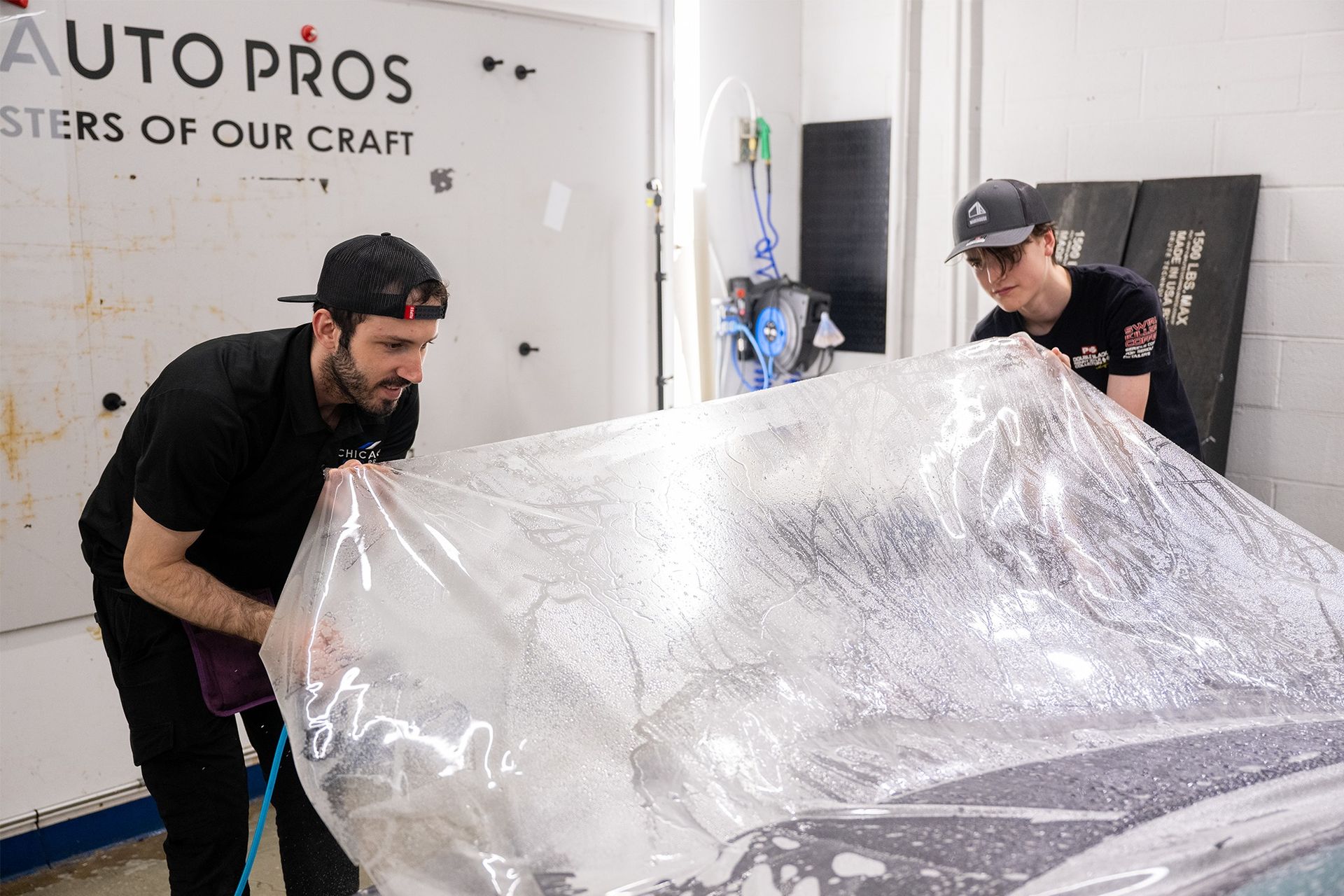Two men are wrapping a car in plastic.