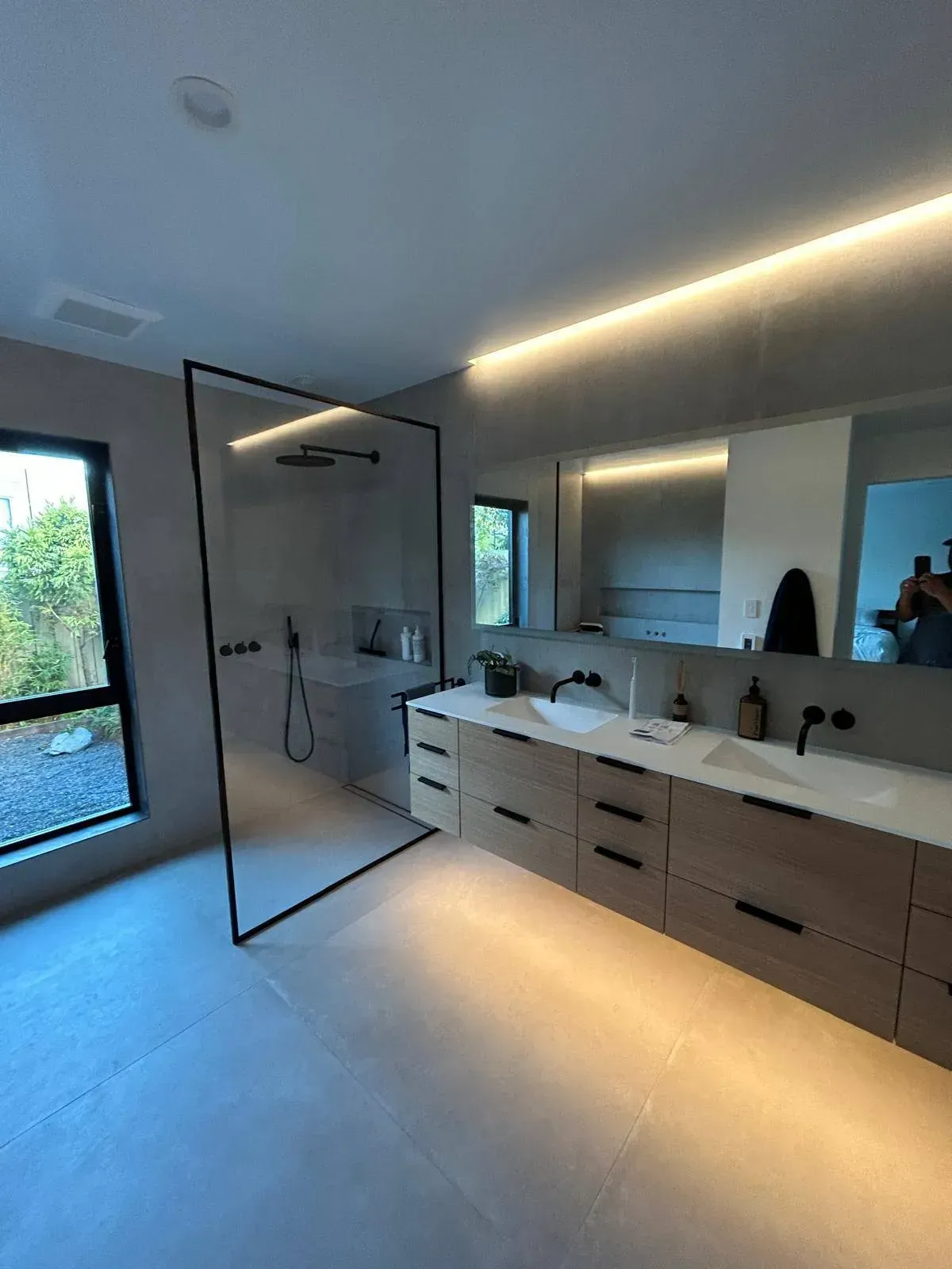 Modern bathroom with glass shower, wooden vanity, and long mirror.