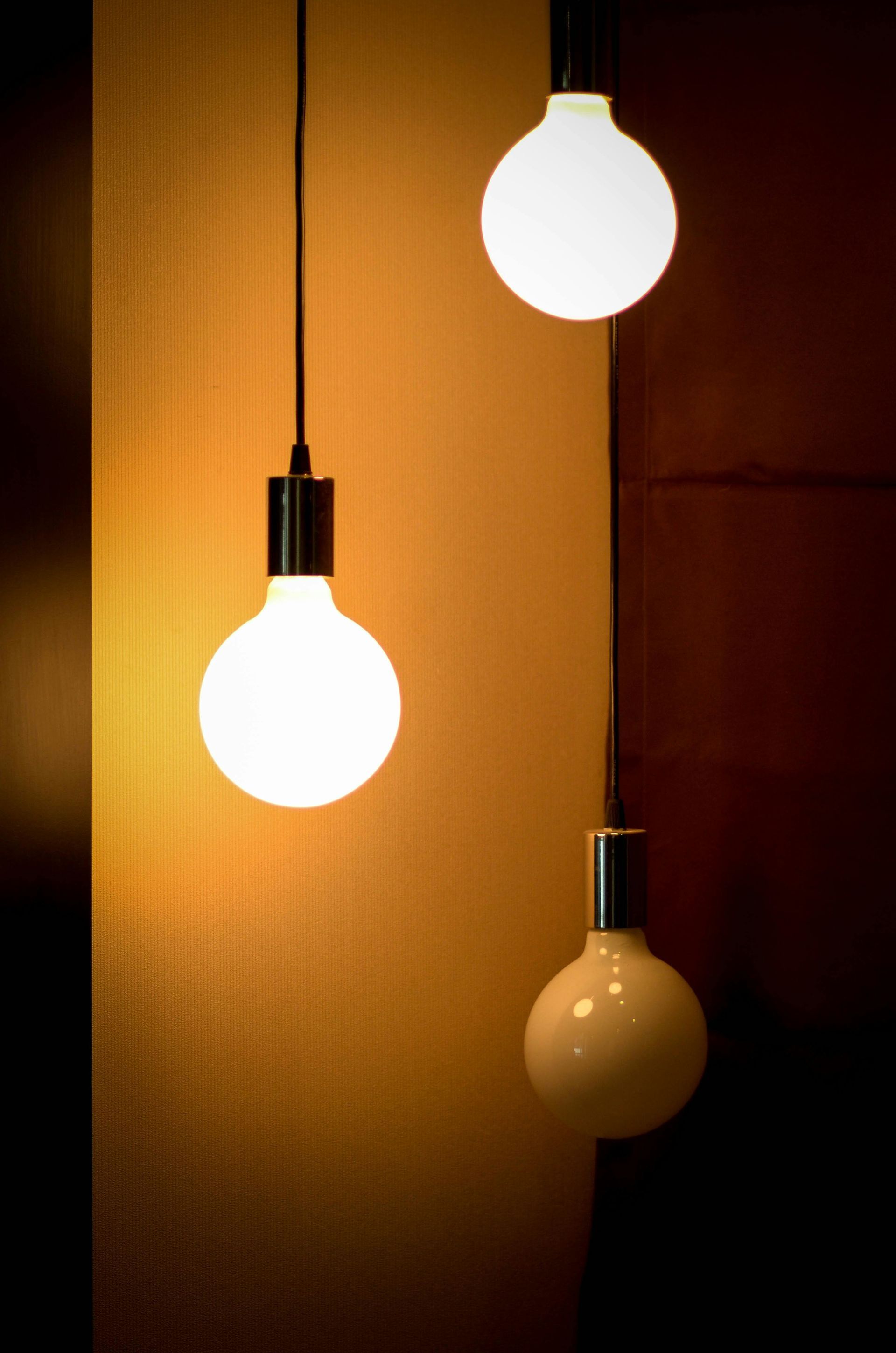 Three lit, round light bulbs hanging from the ceiling; two white, one off-white. Yellow and brown background.