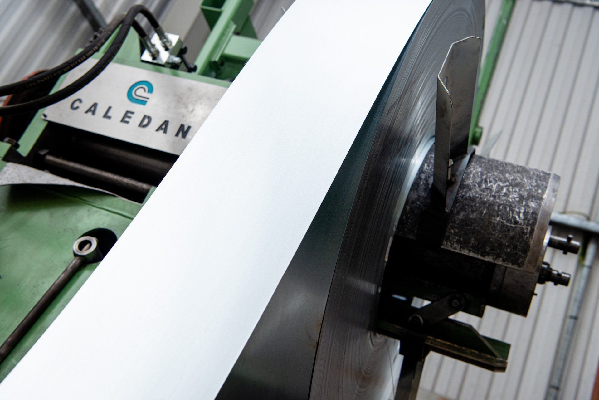 Coiled metal sheet unwinding from a CALEDAN machine, in an industrial setting.