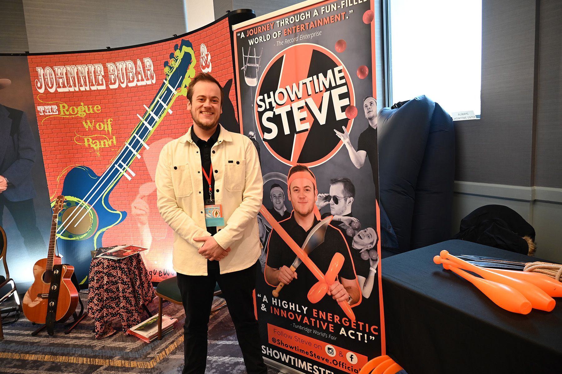 A person in a cream jacket stands at a booth for 'Showtime Steve' next to orange juggling clubs and a guitar display.
