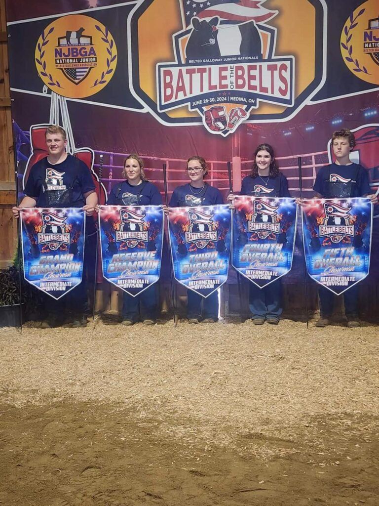 Five people stand in a line holding championship banners at a 'Battle of the Belts' event, in front of a branded backdrop.