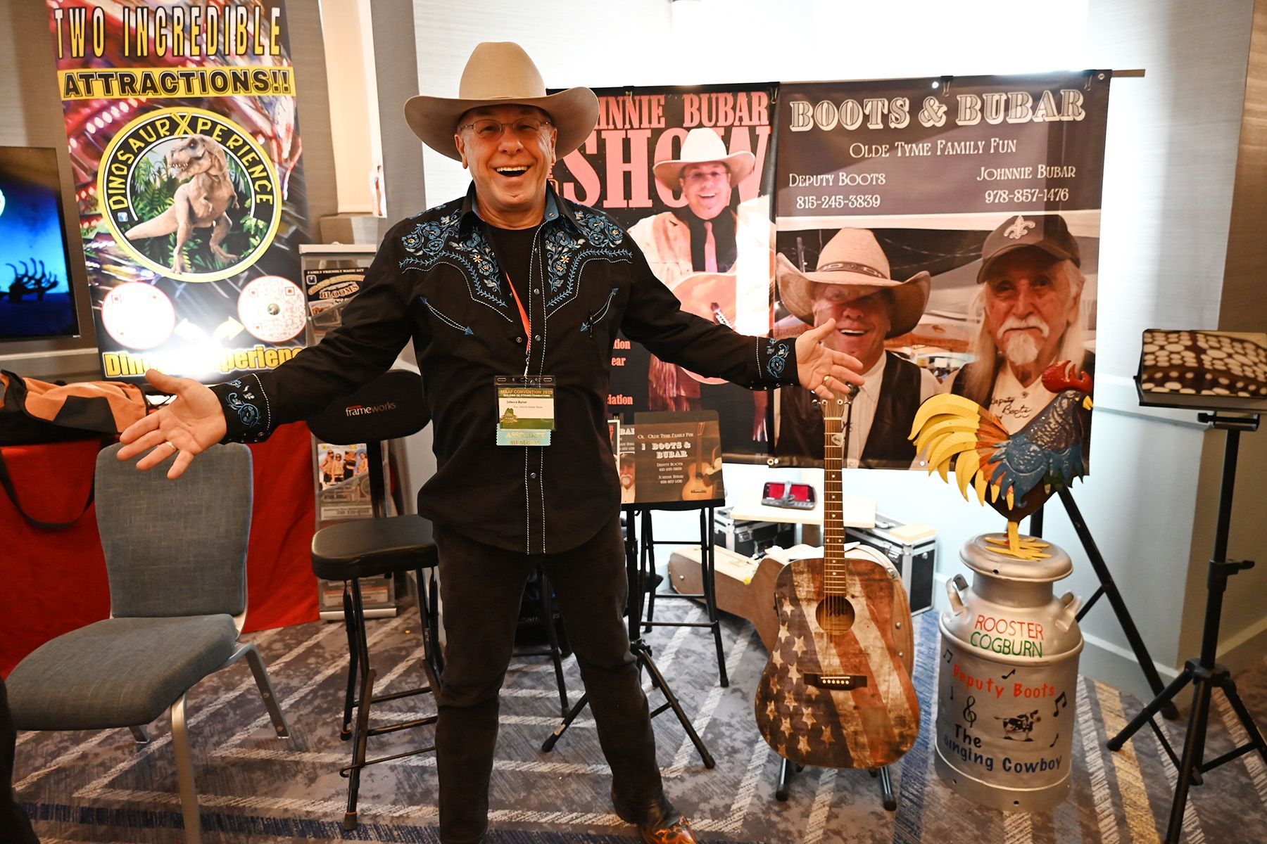 A smiling person in a cowboy hat and black shirt stands at an event booth with signs for the 'Boots & Rubar Show.'