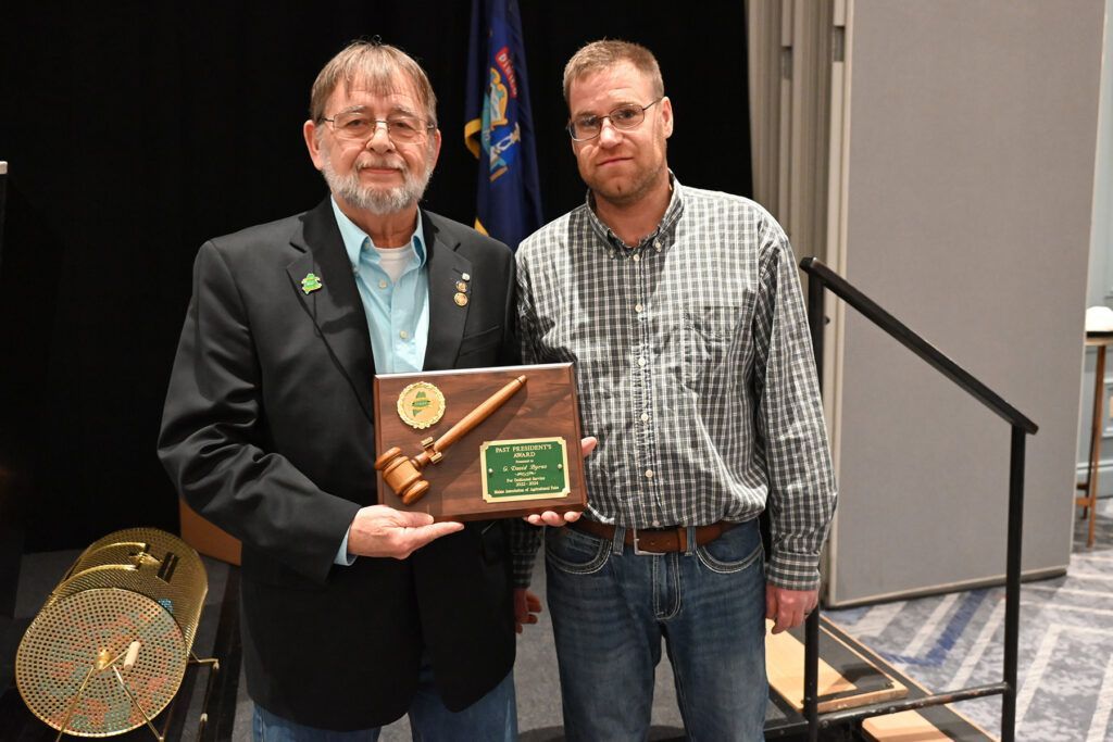 Two men standing side-by-side, one holding a commemorative plaque with a gavel emblem.