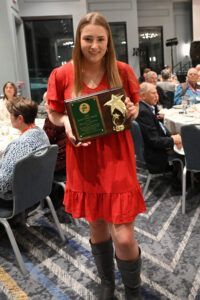 A person in a red dress holding an award plaque at a banquet.