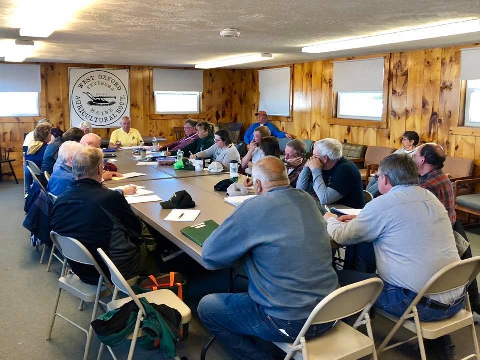 A group of people sits around a long table in a wood-paneled room for a meeting at the West Milford Fish and Game Club.
