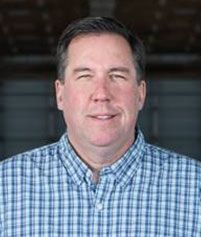 A professional headshot of a person wearing a blue and white checkered button-down shirt, centered against a dark background.