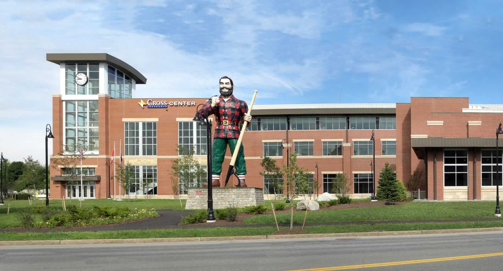 A large Paul Bunyan statue stands in front of a modern brick building under a clear blue sky.