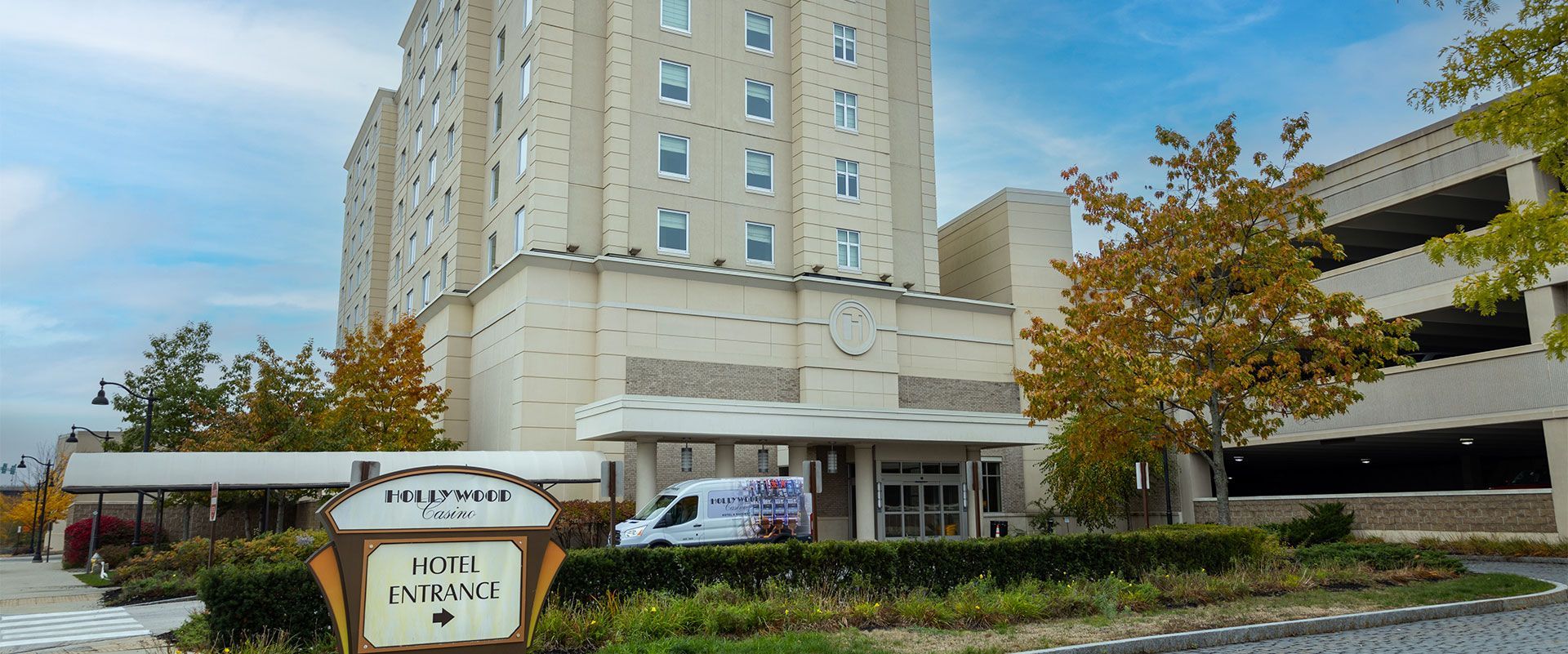 The entrance of the light-colored stone Lockwood Hotel with an adjacent parking garage under a bright blue sky.