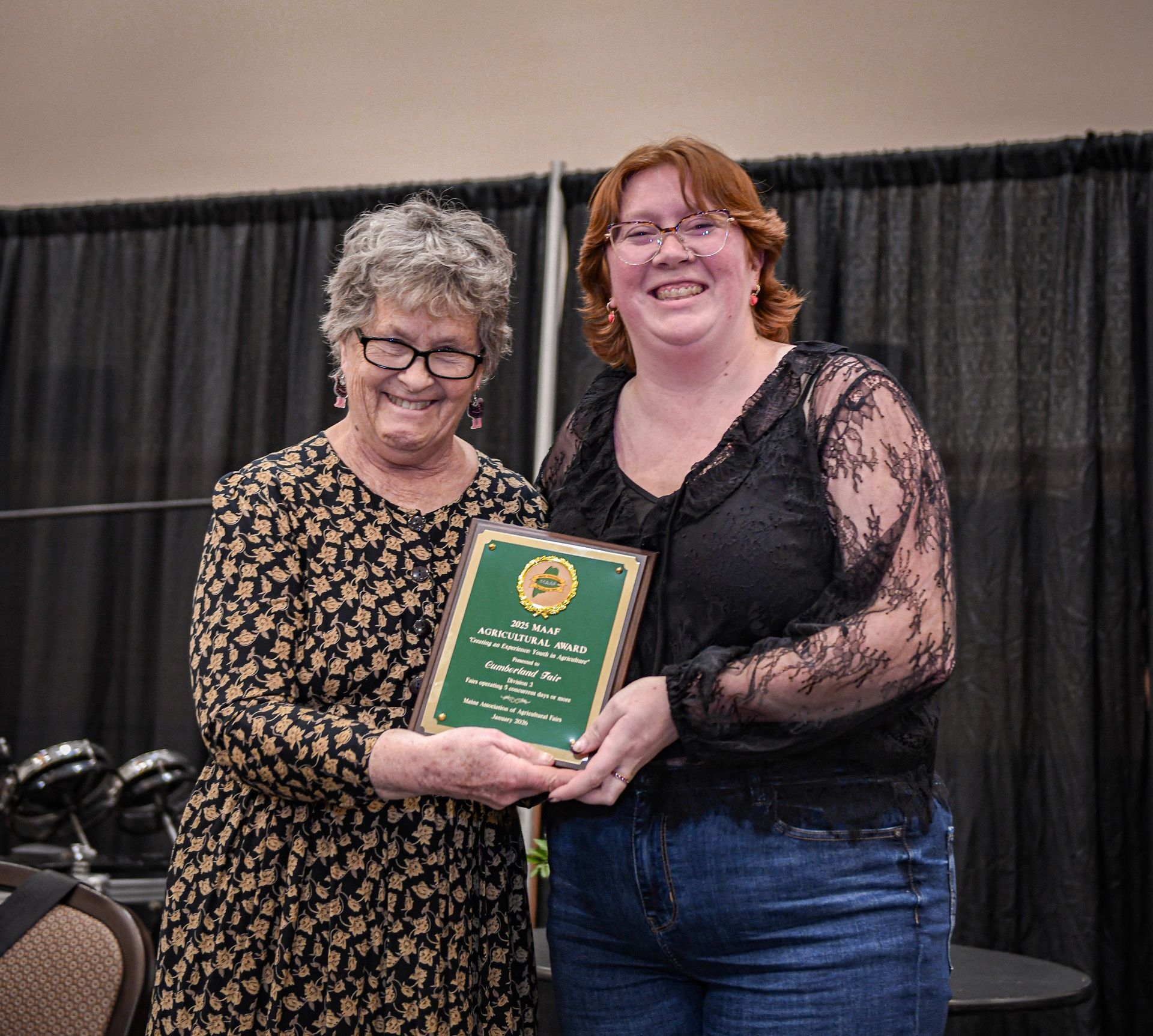 Three people standing on a stage at a conference, with one person holding an award plaque next to a 50/50 raffle sign.