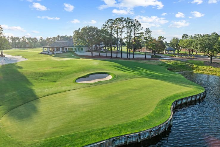 Golf green beside water with sand bunker and clubhouse in the background