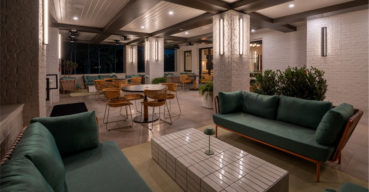 Modern indoor lounge with green sofas, tables, and warm ceiling lights.