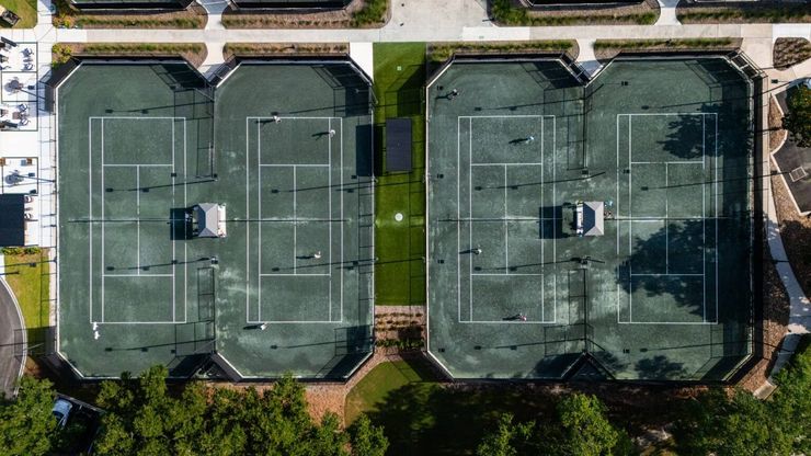 Aerial view of two adjacent rooftop tennis courts with green surfaces and surrounding trees.