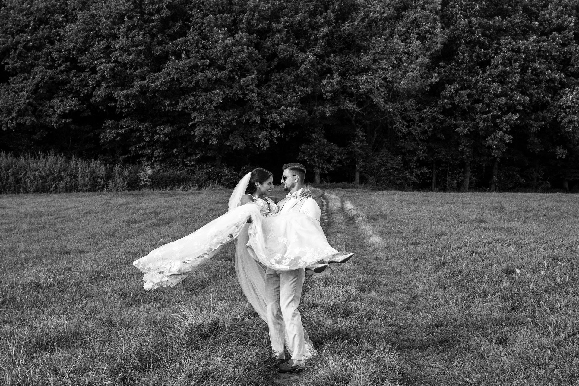 Bräutigam trägt Braut auf Wiese – emotionale Paarfotos in der Natur