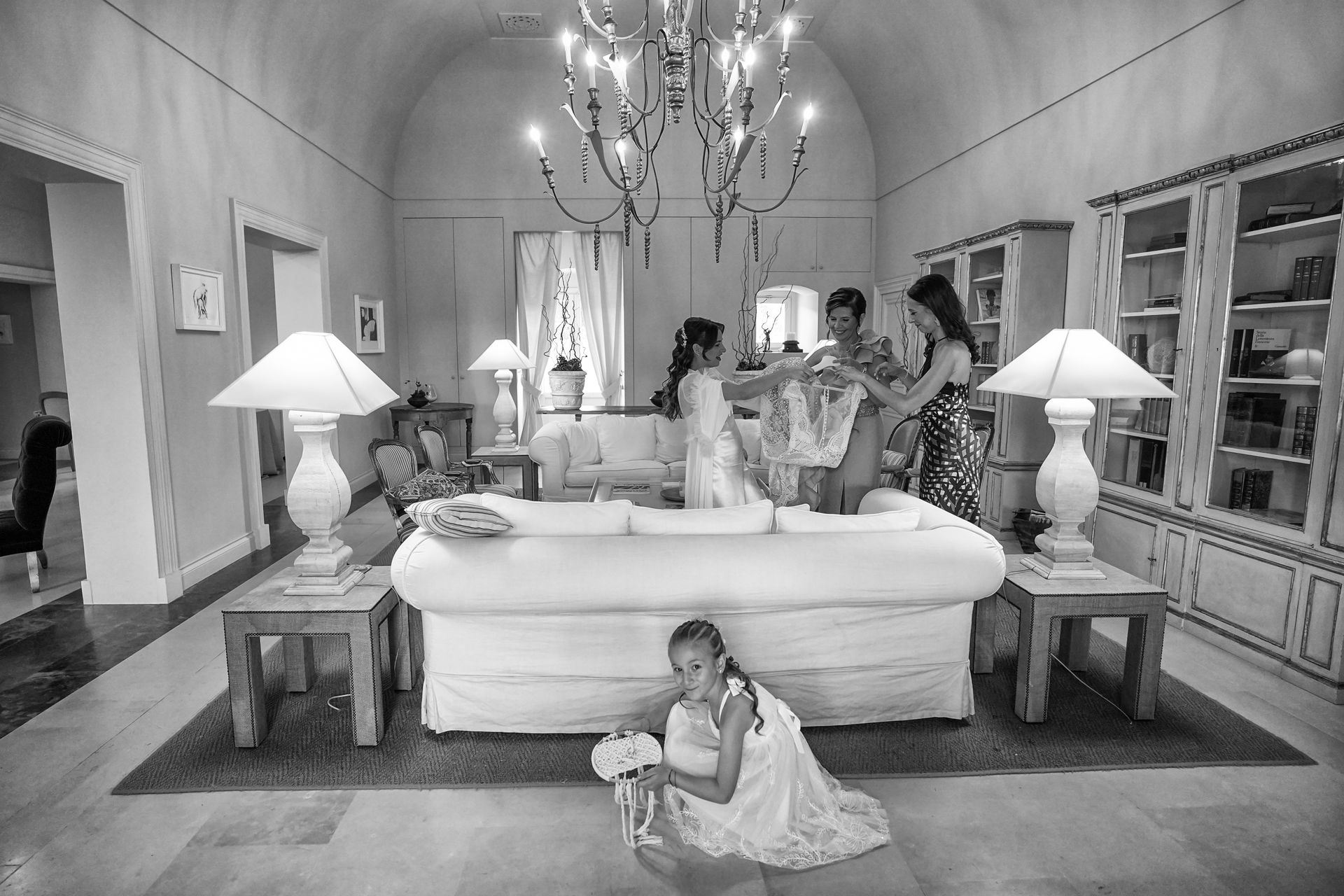Blumenmädchen kniet vor Couch und versteckt sich vor dem Foto, Hochzeitsvorbereitungen im Hintergrund – familiäre Momente Hochzeit NRW