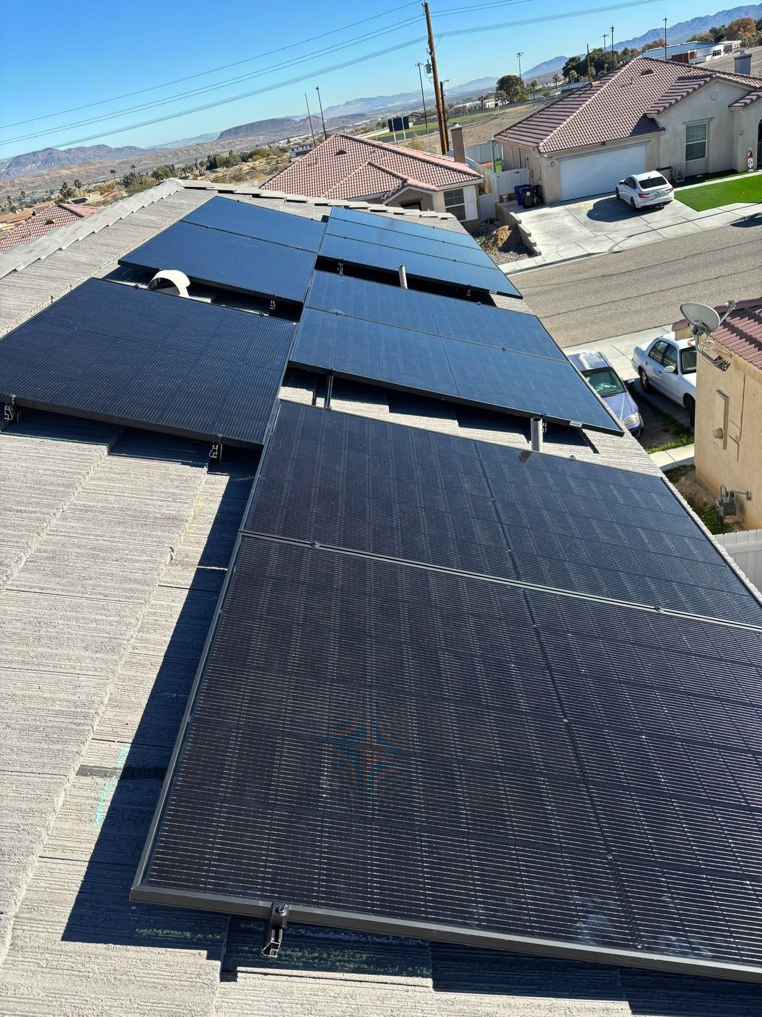 Rows of dark solar panels on a rooftop in bright sunlight with neighborhood houses in the background