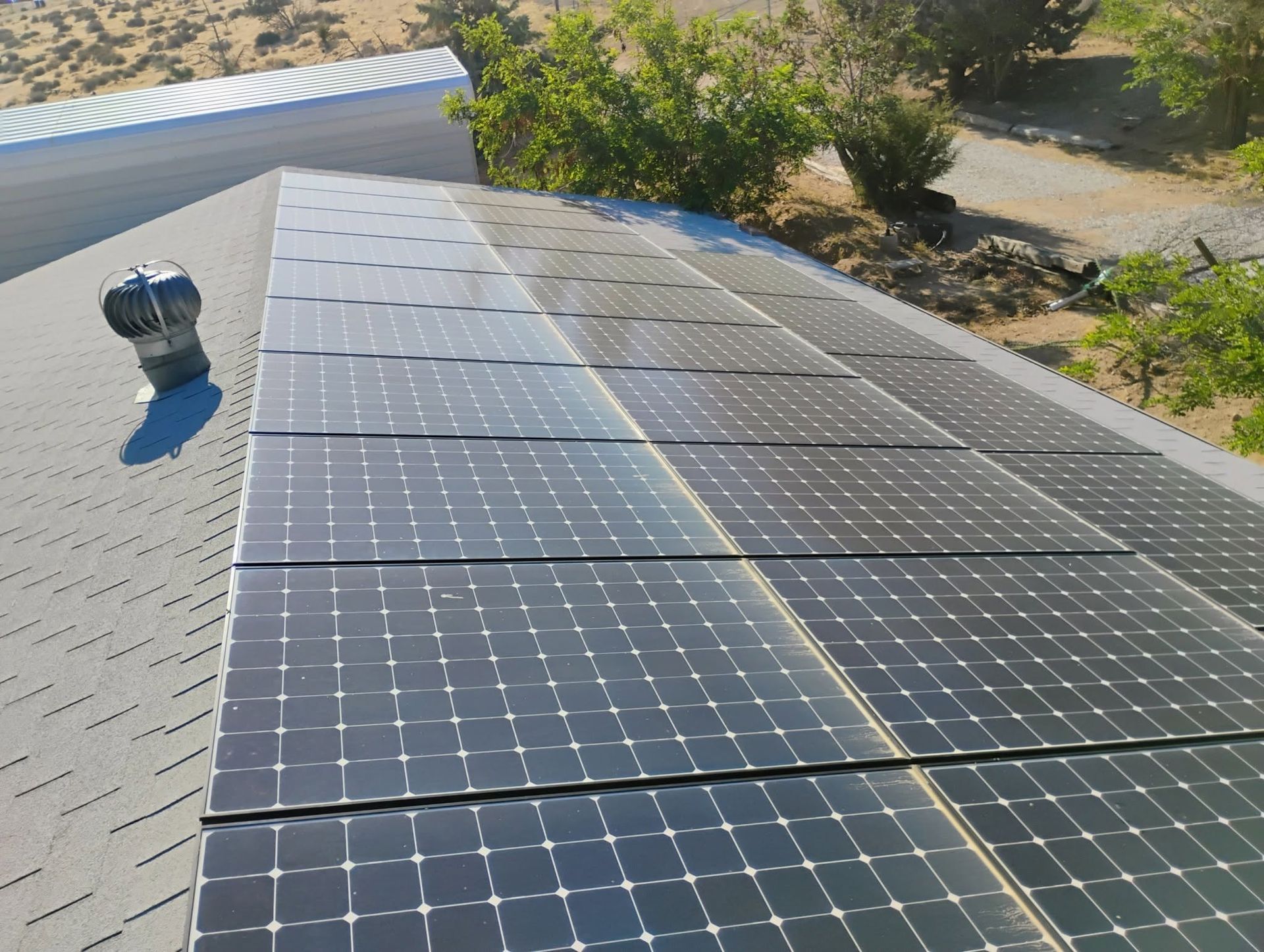 Solar panels on a gray shingled roof with a rooftop vent, viewed from above.