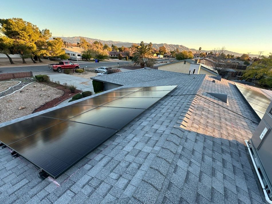 Rooftop solar panels on a shingled roof at sunset, with trees and hills in the background