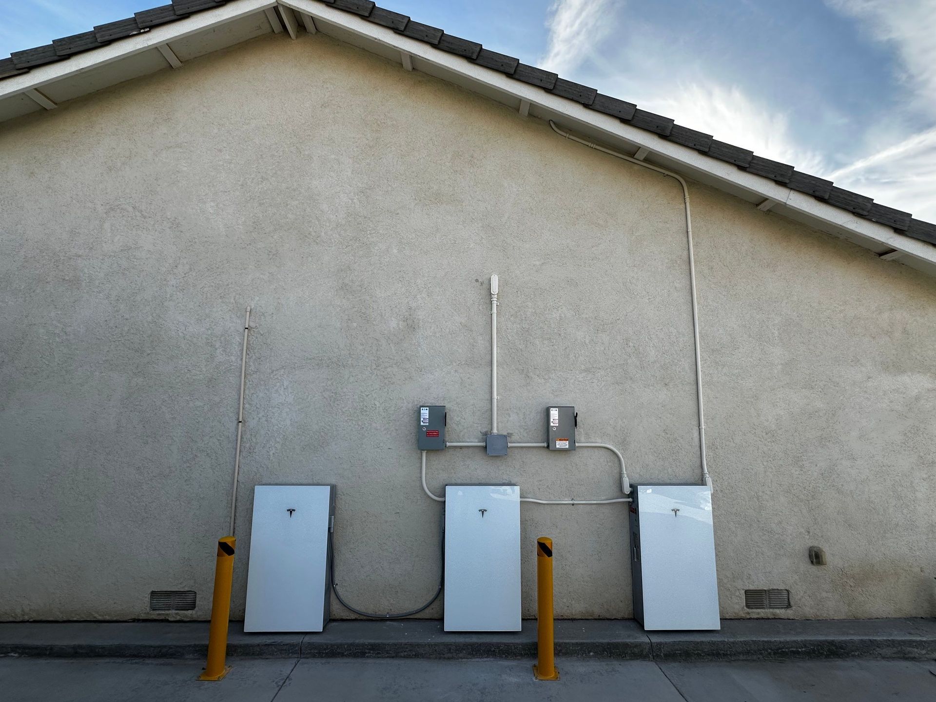 Two white utility boxes mounted on a stucco wall outdoors under a roof eave
