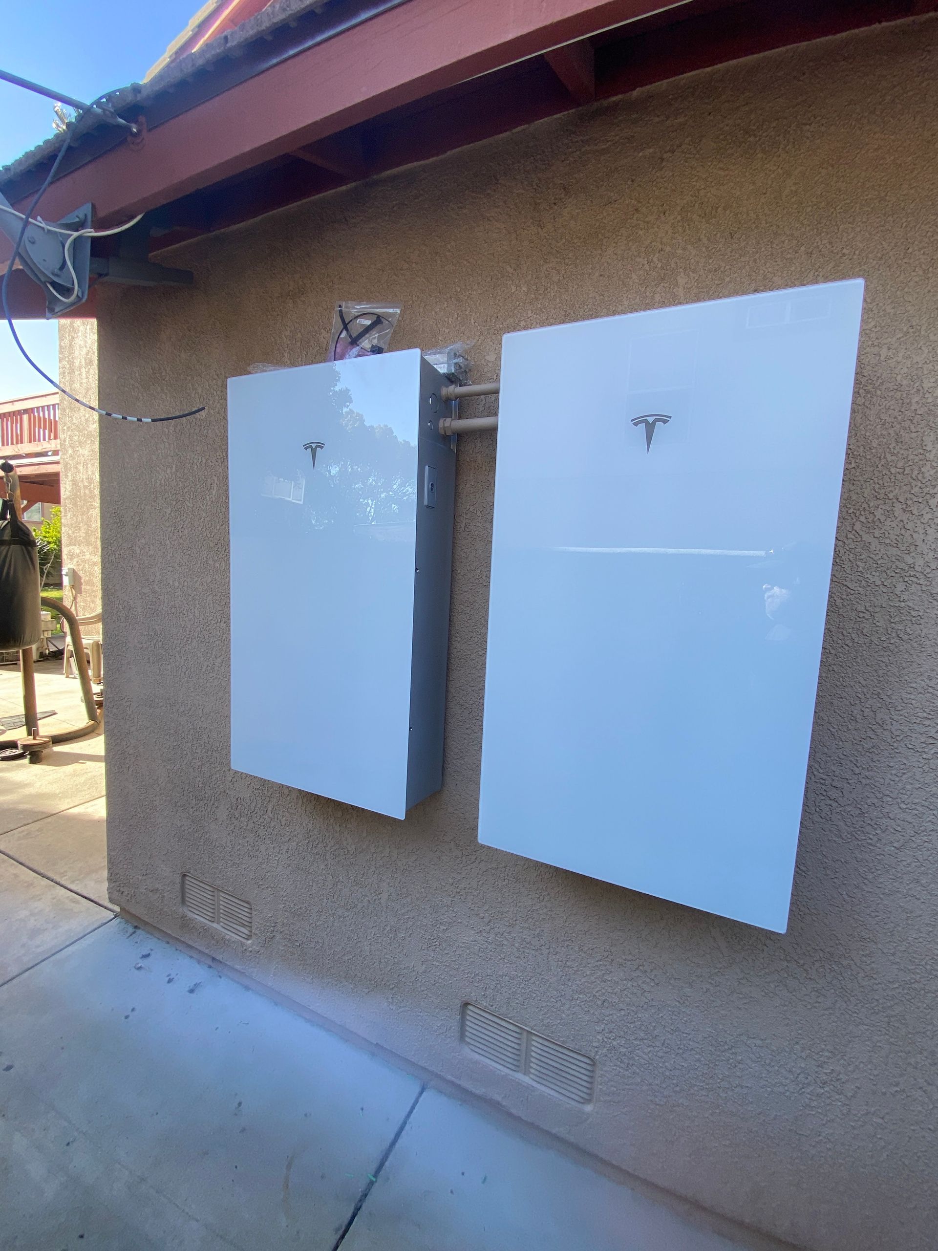 Two white wall-mounted utility boxes on a stucco exterior wall under a roof overhang.