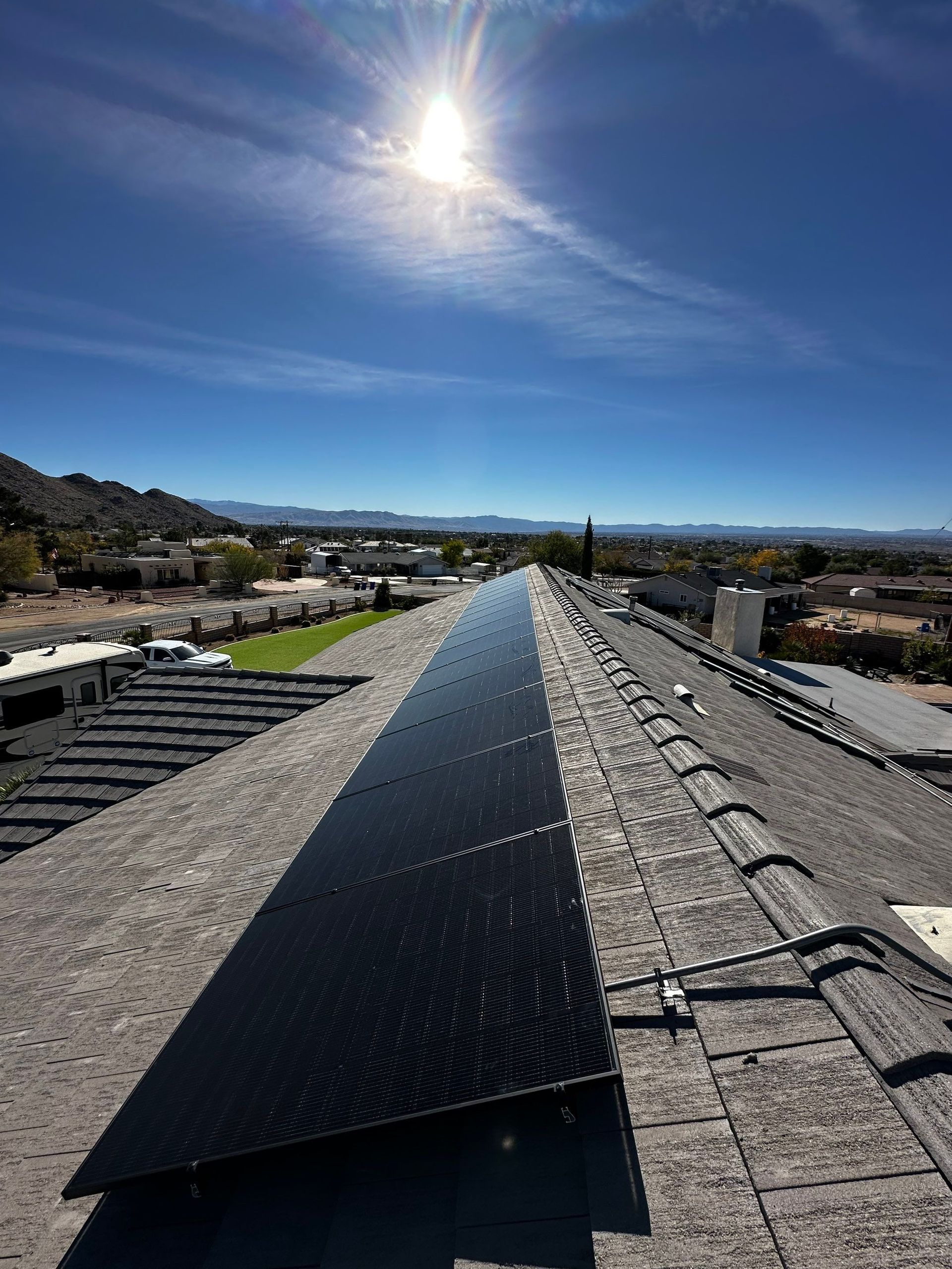 Rooftop solar panels under a bright sun, overlooking a suburban neighborhood and distant hills.