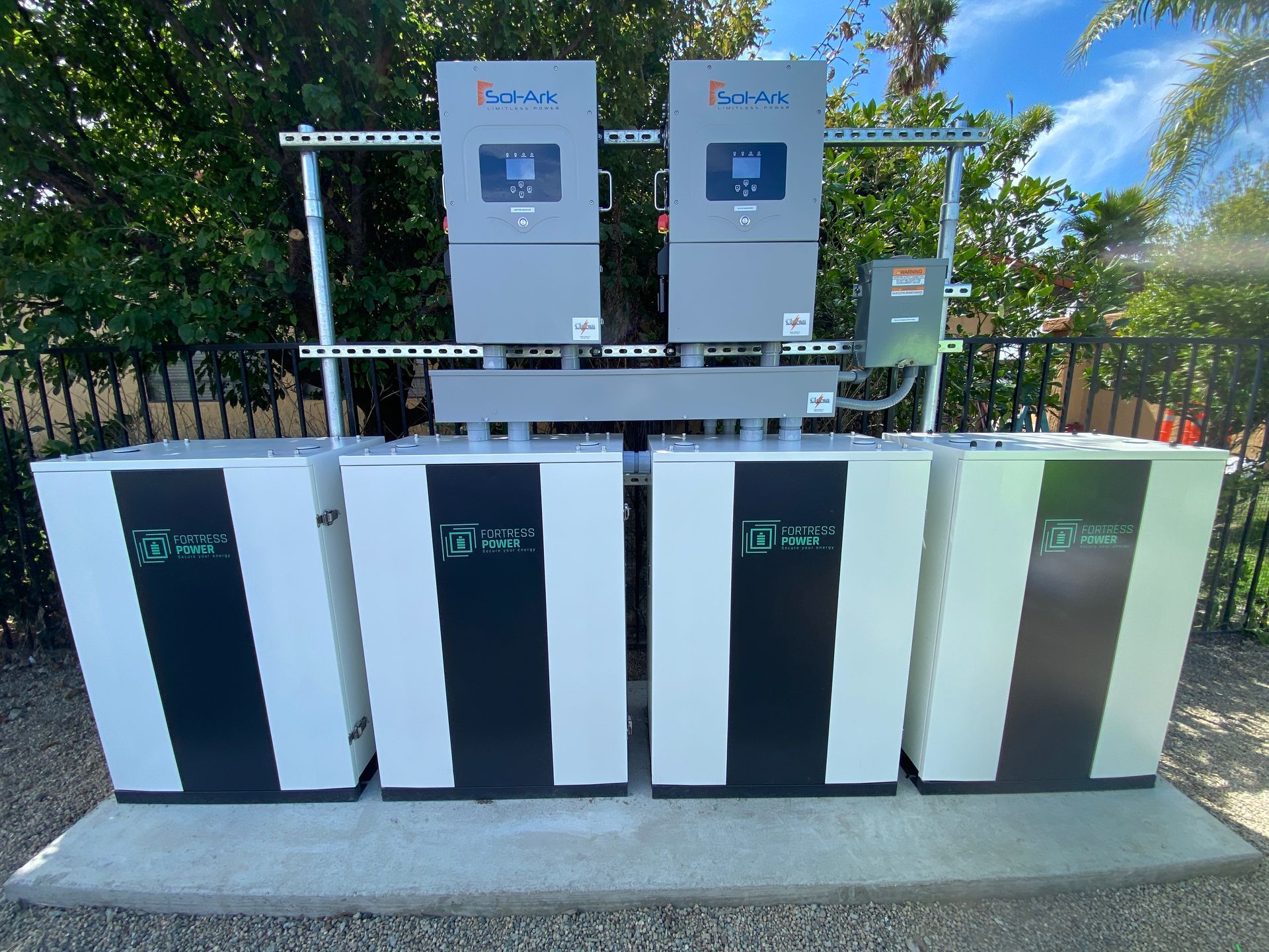 Row of solar battery cabinets and inverters installed outdoors on a concrete pad under a sunny sky