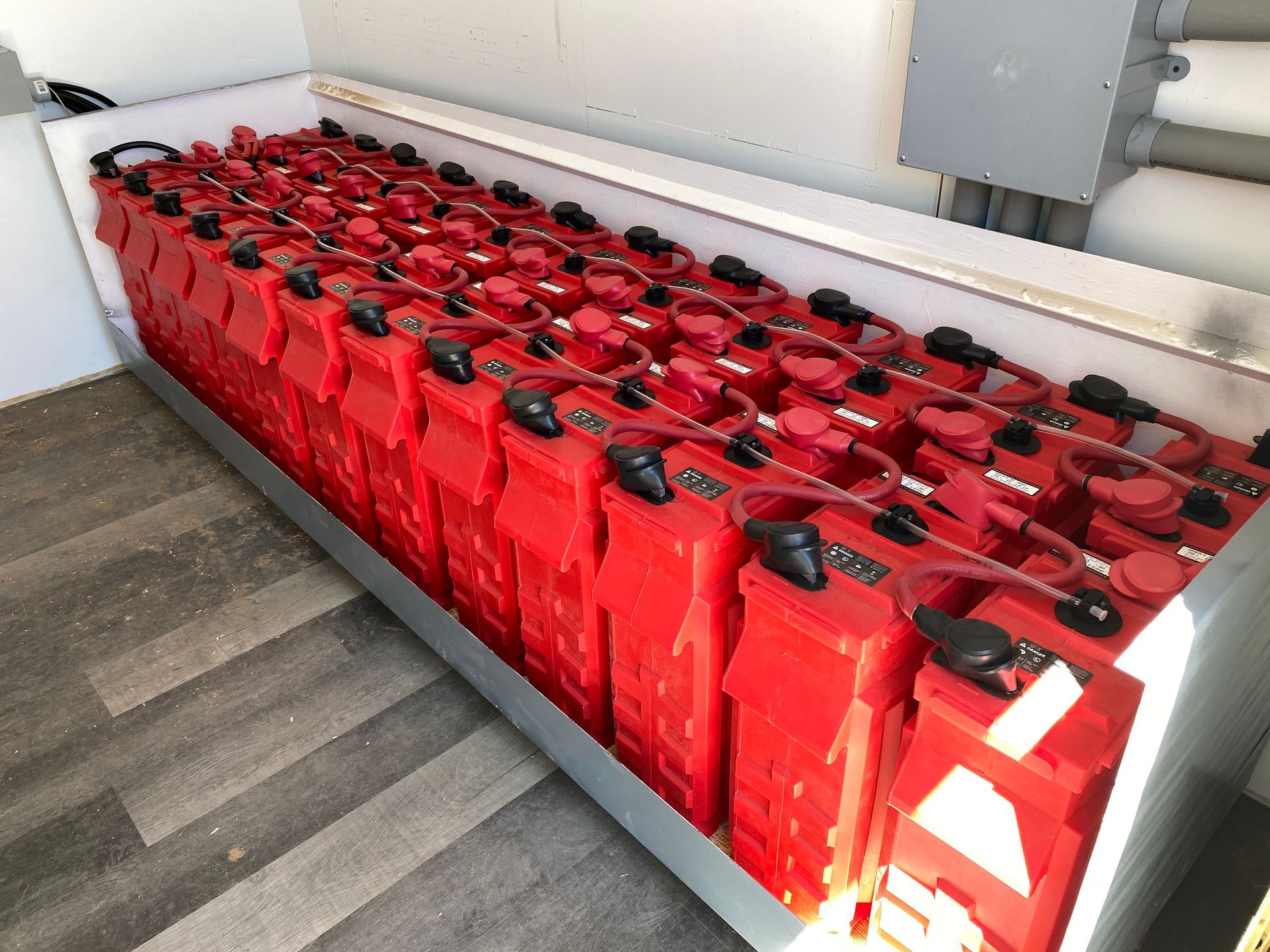 Rows of red fuel cans stacked in a storage area beside a metal wall and concrete floor