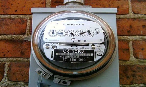 Close-up of a round electric meter mounted on a wall with a brick background.