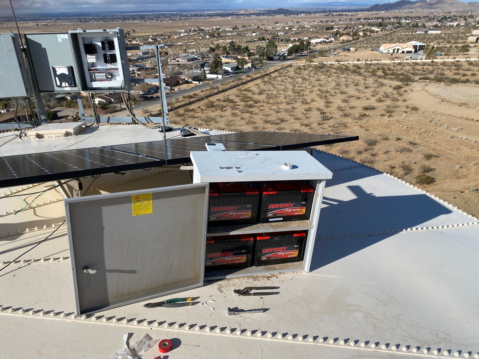 Open electrical cabinet with red battery units on a rooftop near a desert landscape.