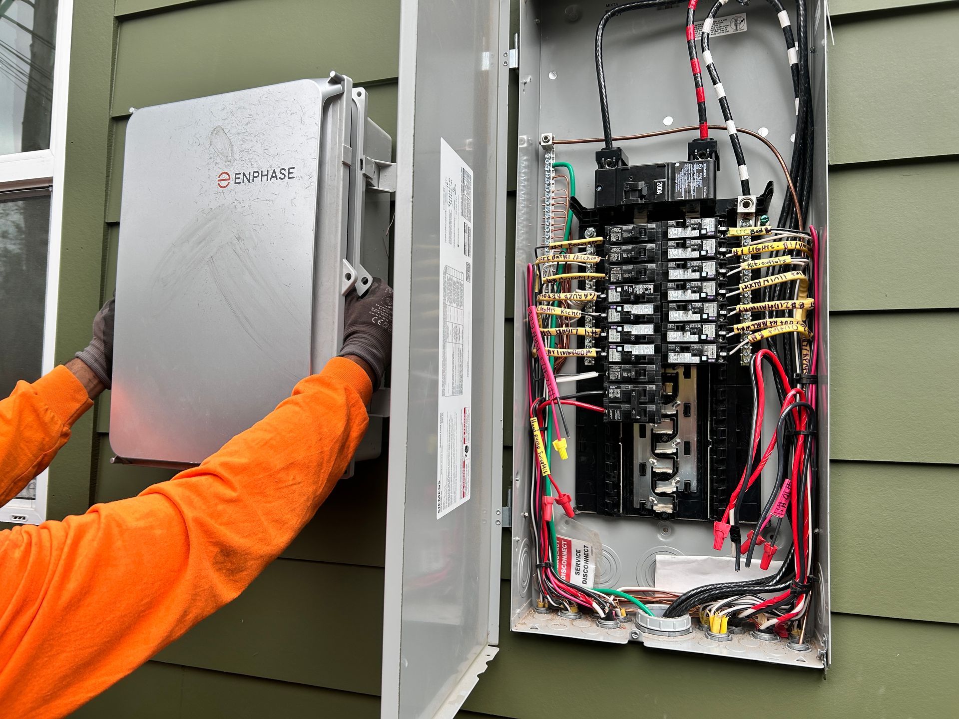 Electrician closing an open outdoor electrical panel with exposed wiring and breakers