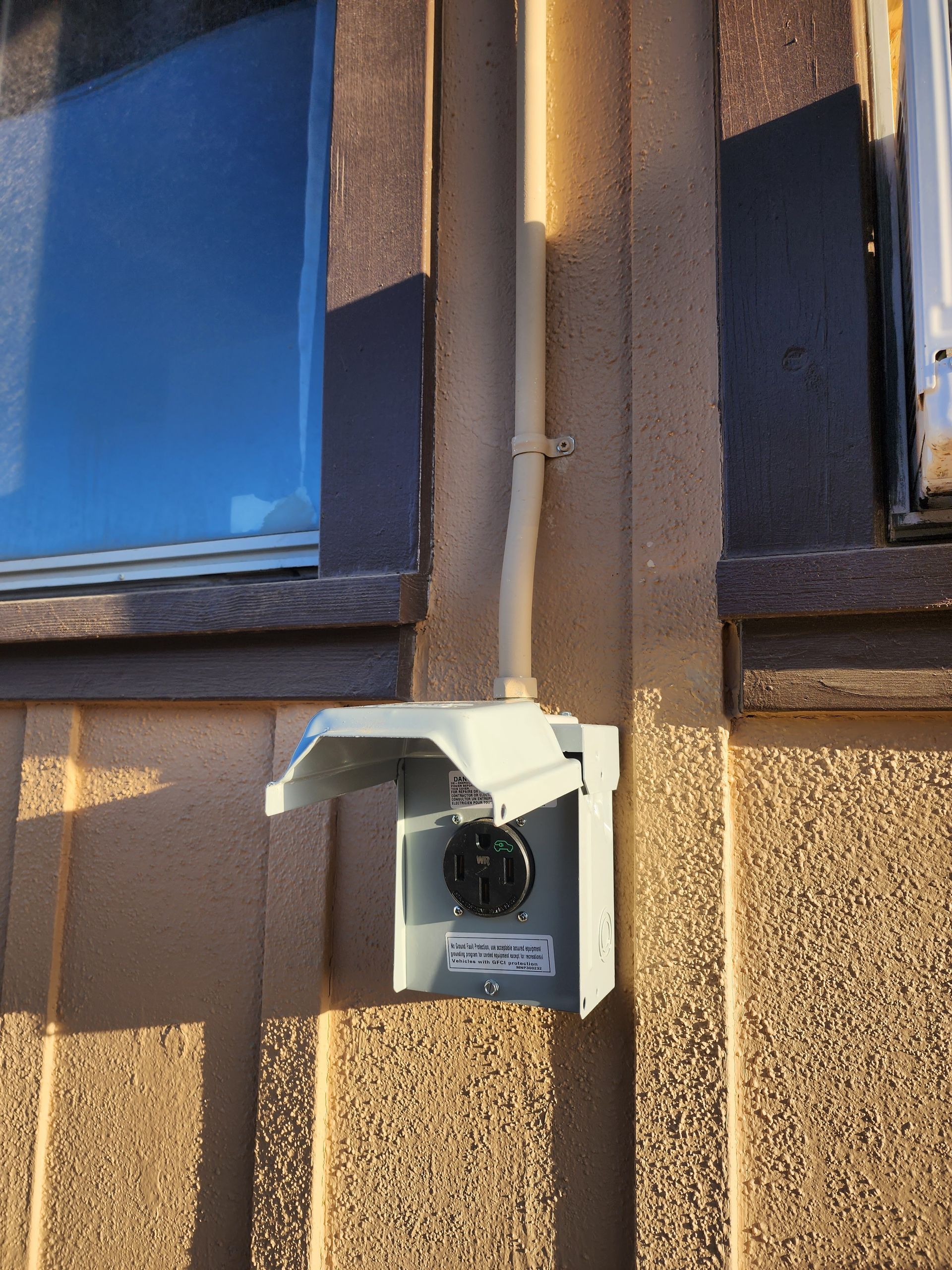 White security camera mounted on a tan stucco wall between two windows.
