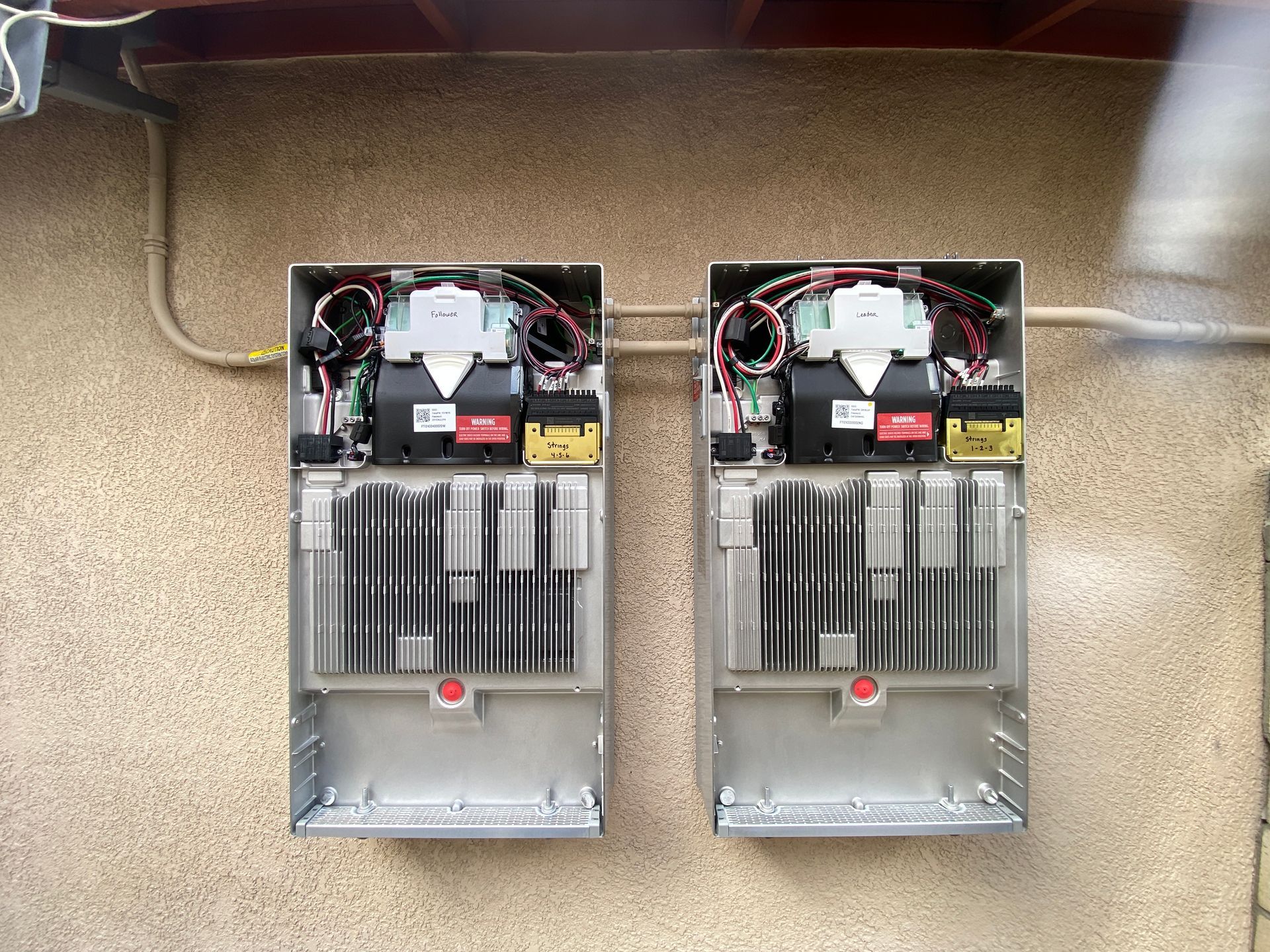 Two open electrical panels mounted side by side on a wall, with wiring and breakers visible.