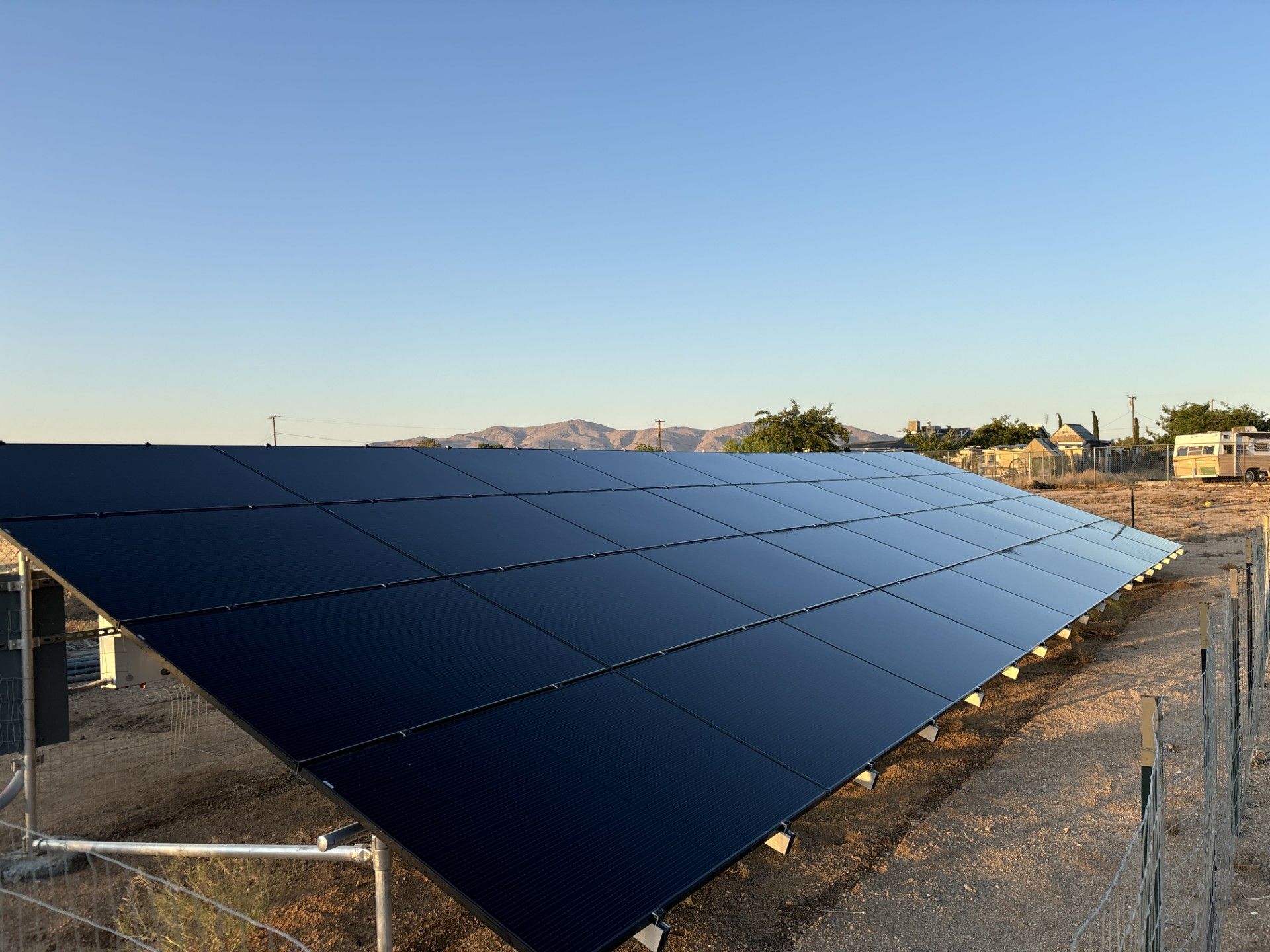 Solar panels in a desert field at sunset with mountains in the distance