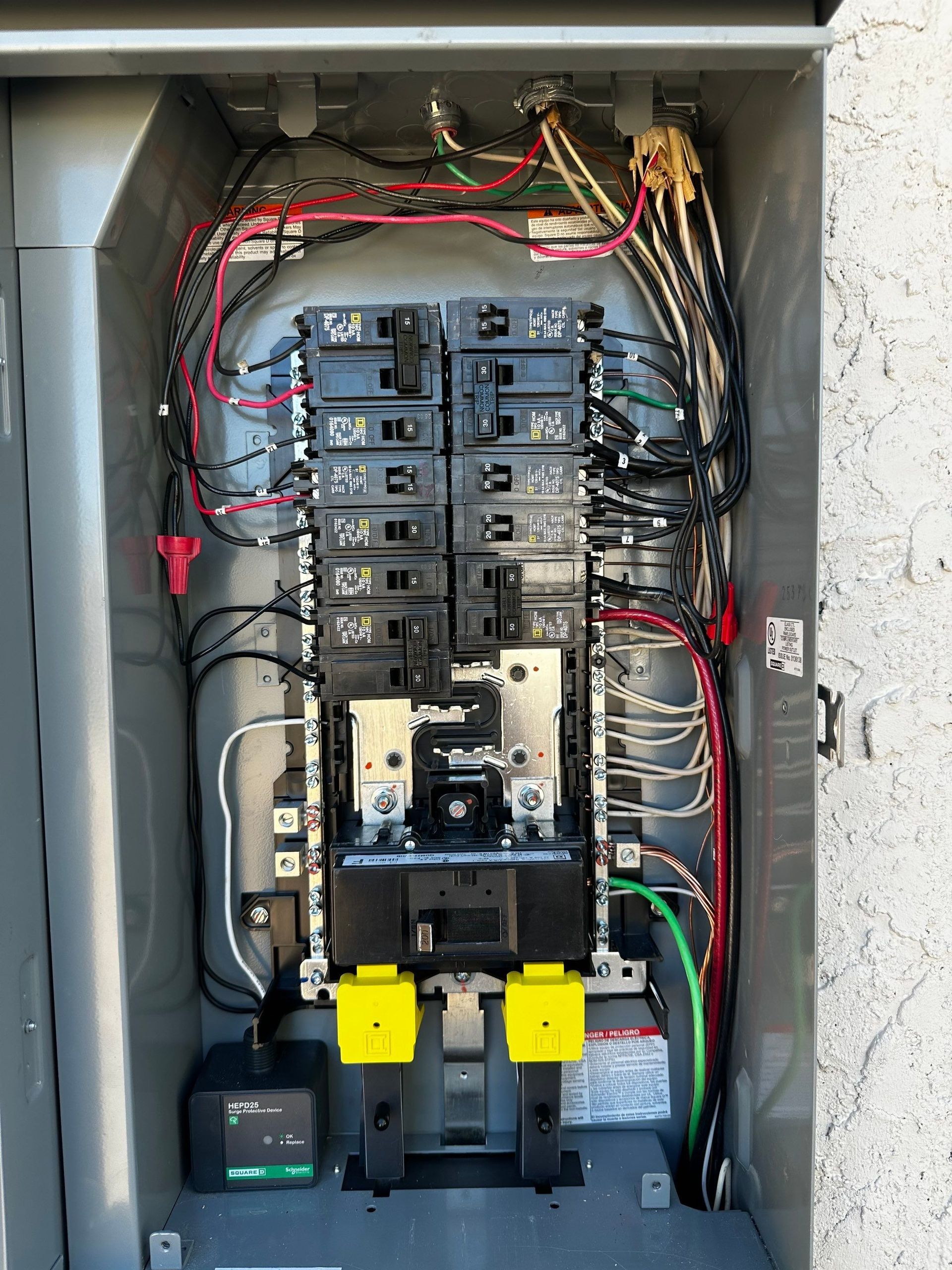 Open electrical breaker panel with wiring, black breakers, and two yellow-handled switches.