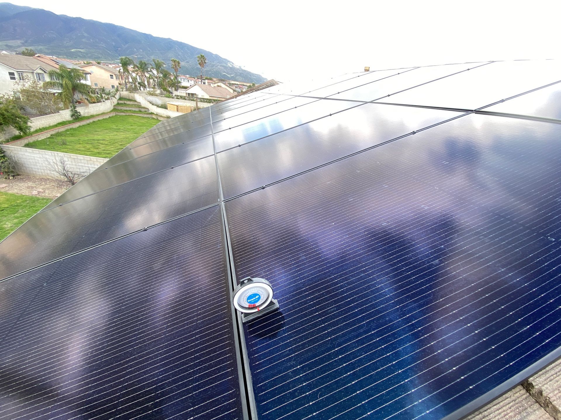 Solar panel array on a rooftop beside a hillside landscape under a cloudy sky