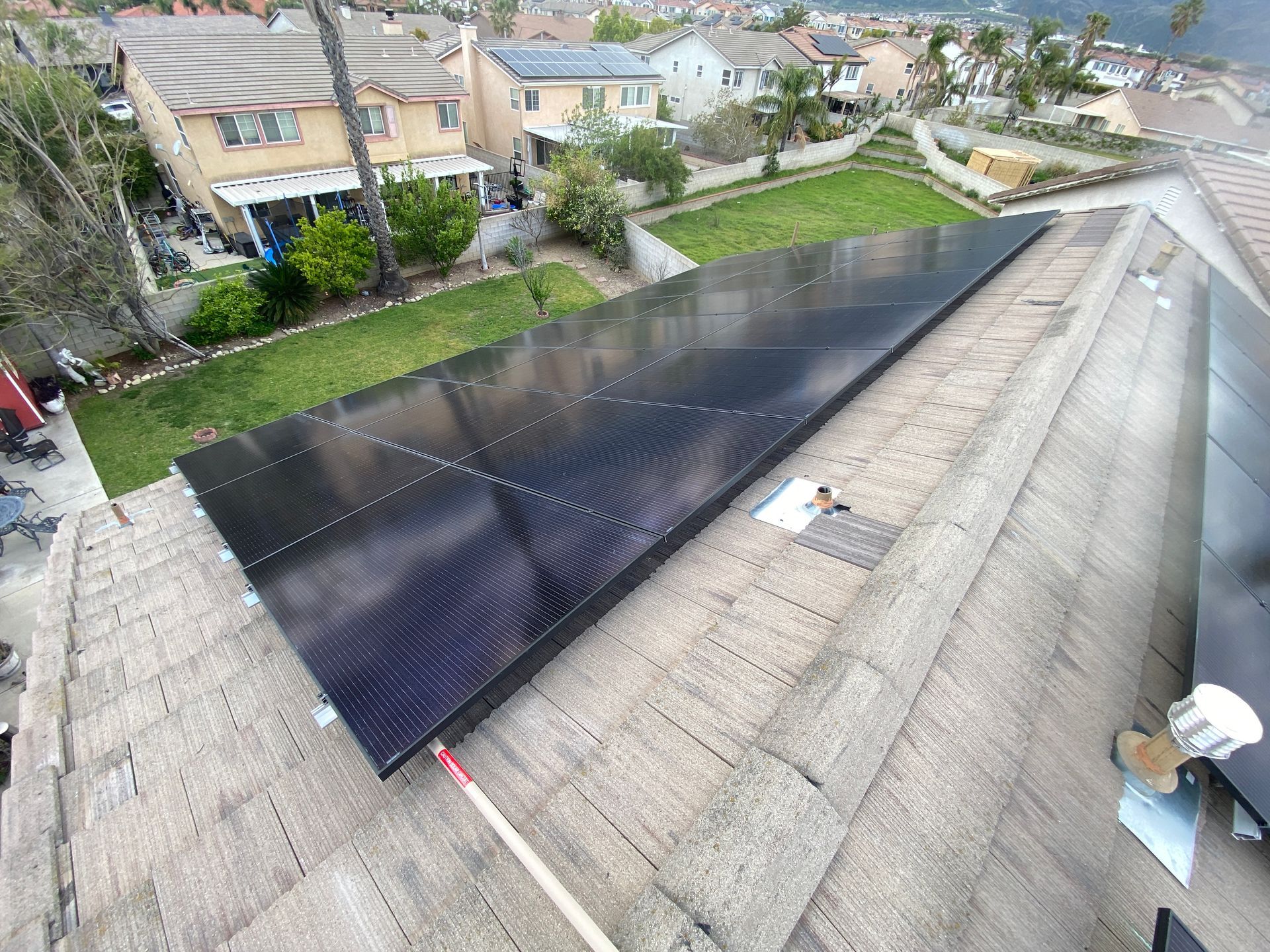Large black solar panel array on a sloped residential rooftop with neighborhood houses in the background