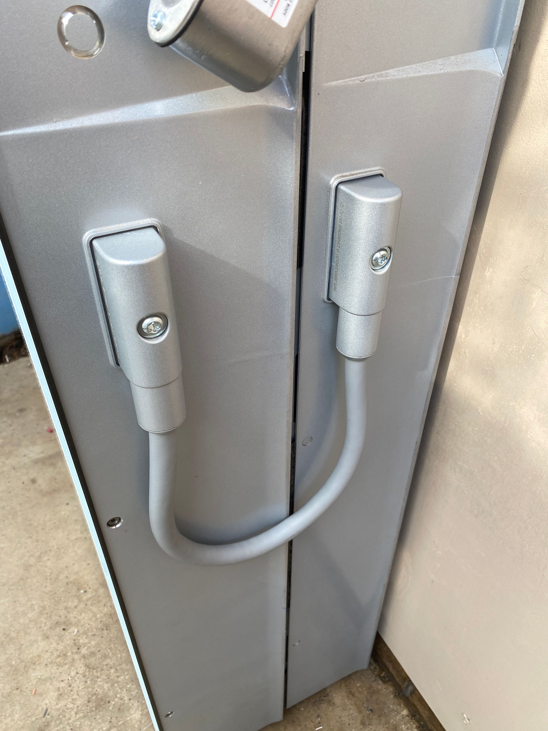 Two gray metal cabinet doors secured by a U-shaped handle and vertical latch locks.