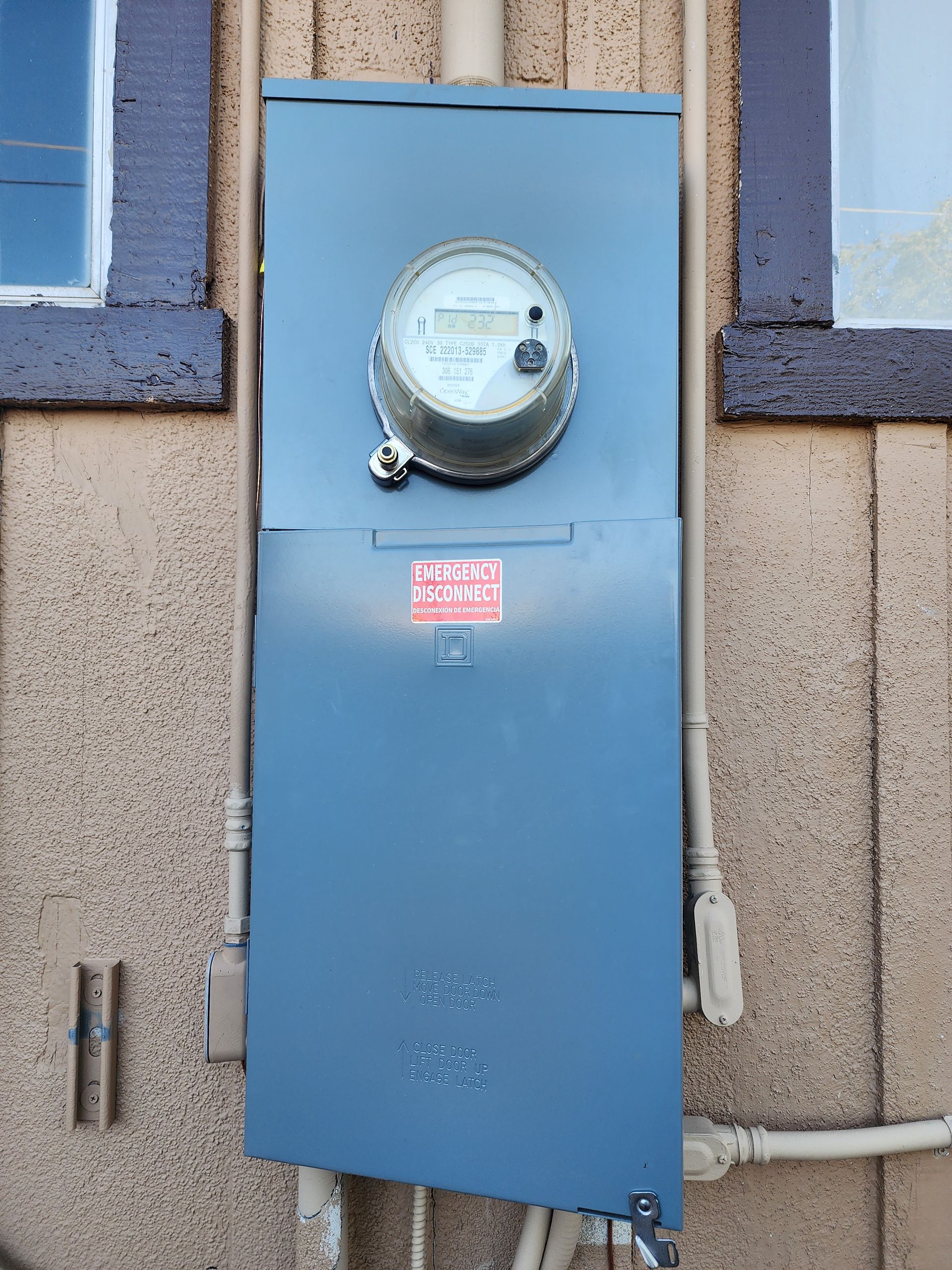 Blue electric meter box mounted on a stucco wall between windows