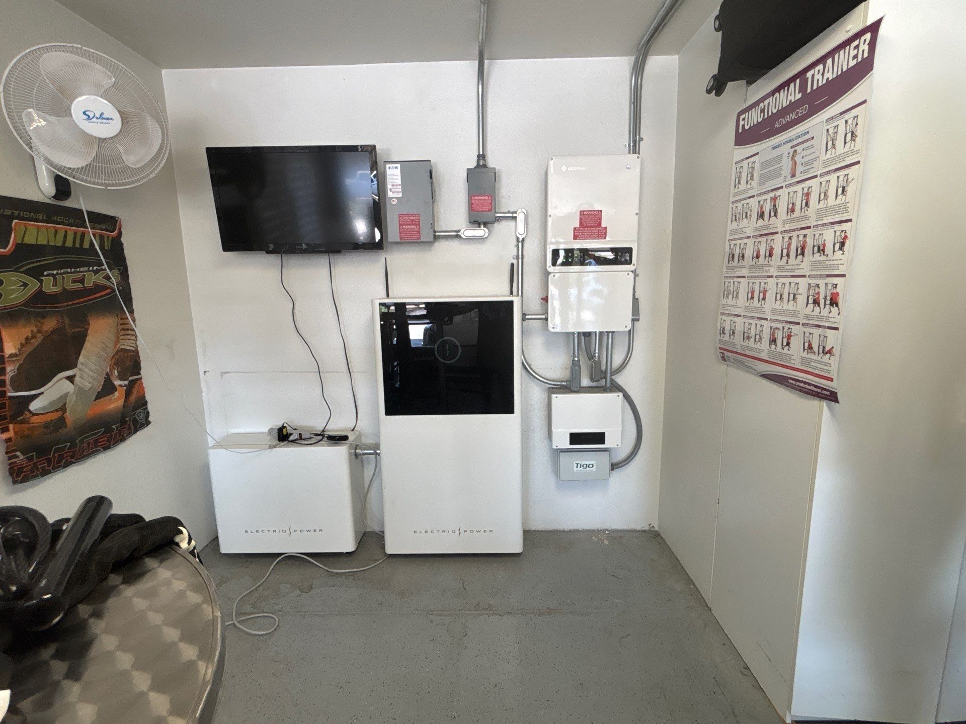 Small utility room with wall-mounted TV, electrical panels, white cabinets, and a safety poster on the right wall