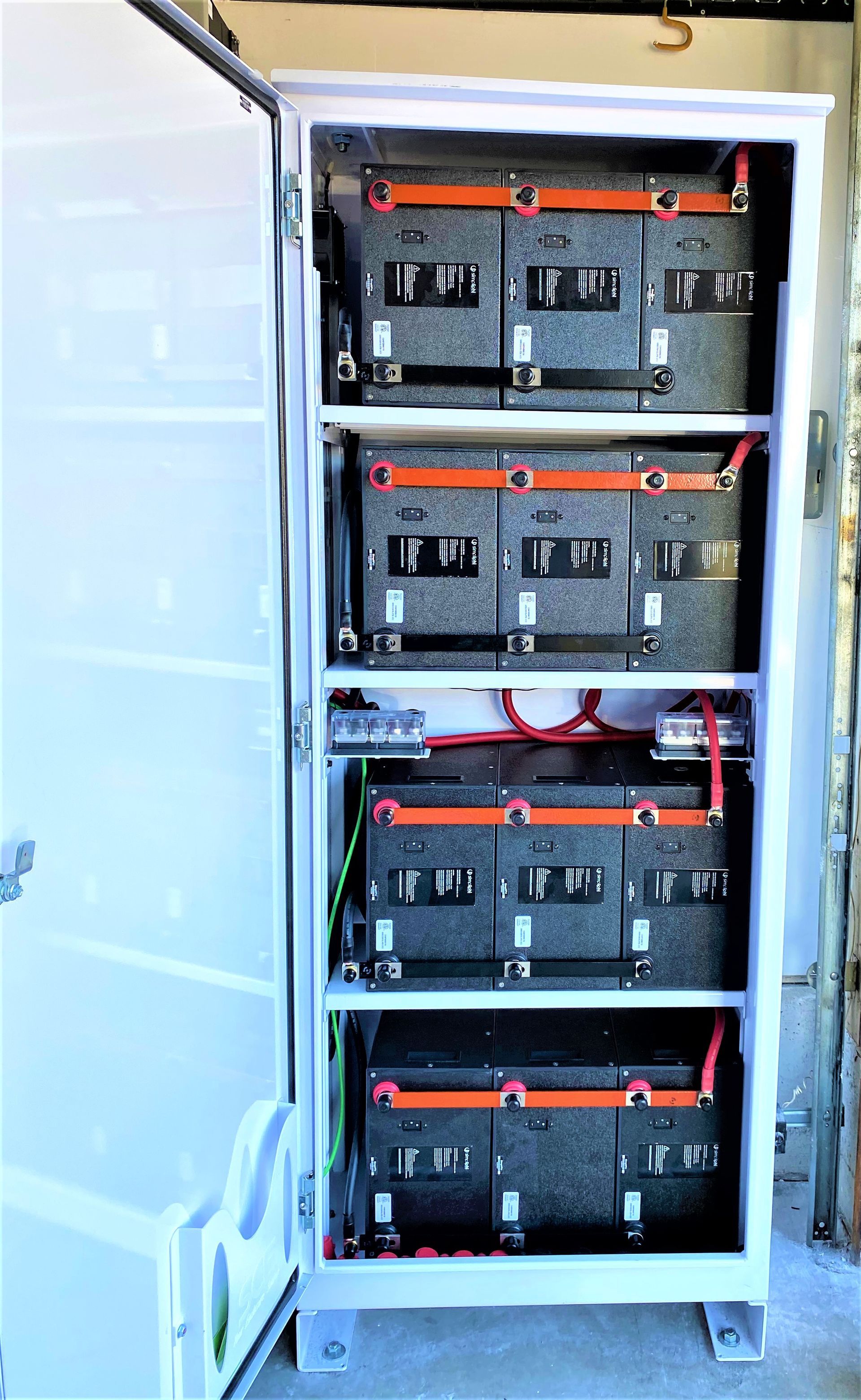 Open electrical cabinet with four stacked black battery/inverter units and orange handles.