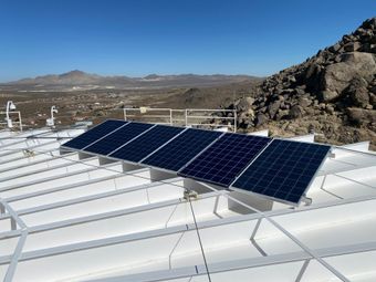 Solar panels mounted on a white rooftop with desert mountains in the background