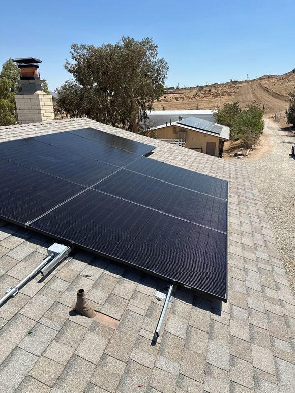 Solar panels on a rooftop in a dry, hilly landscape under a clear sky