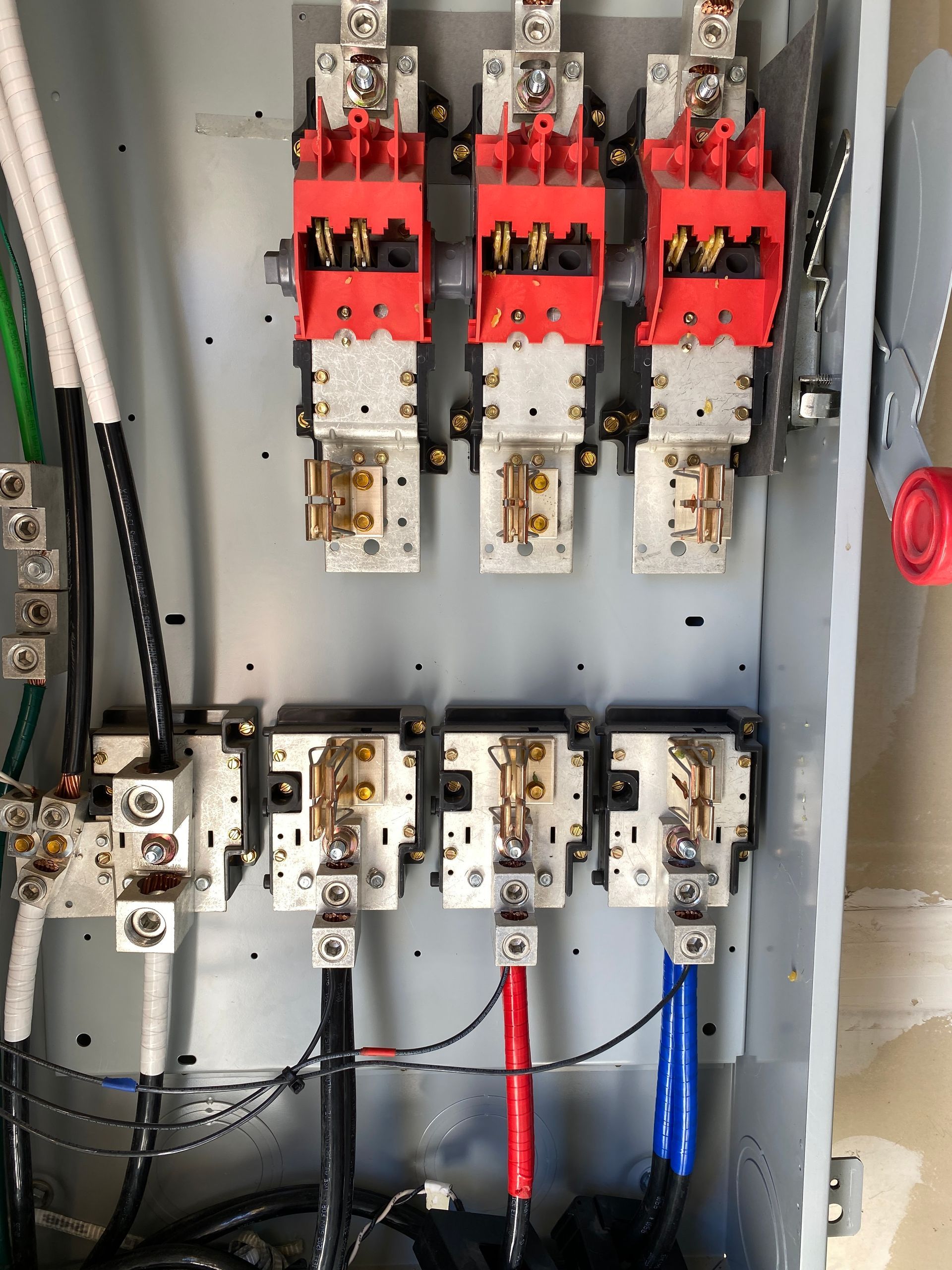 Electrical panel with red and white circuit breakers, wiring, and blue and red cables inside a metal cabinet