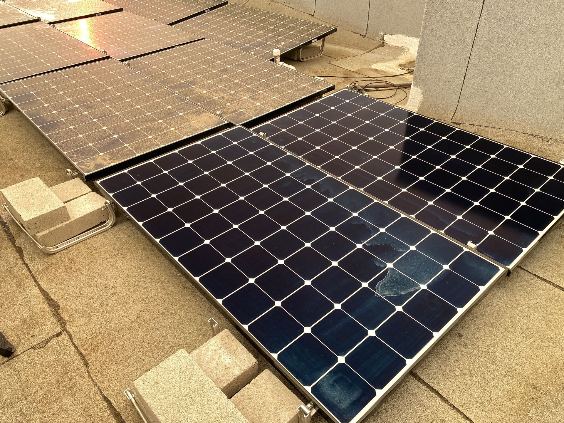 Solar panels laid out on a rooftop, with one dark blue panel in the foreground.