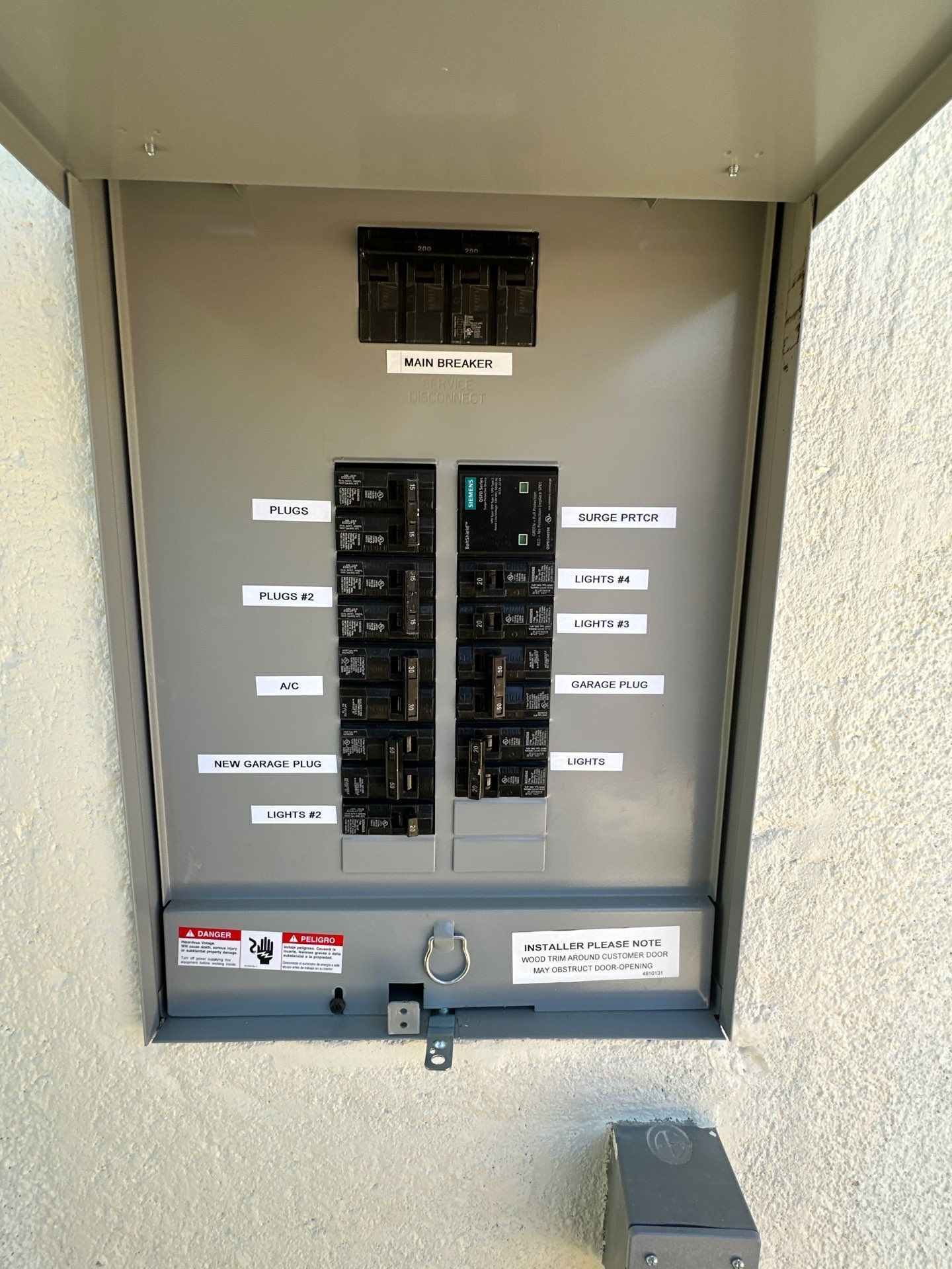 Open electrical circuit breaker panel in a gray metal cabinet with labeled switches and a lower latch.