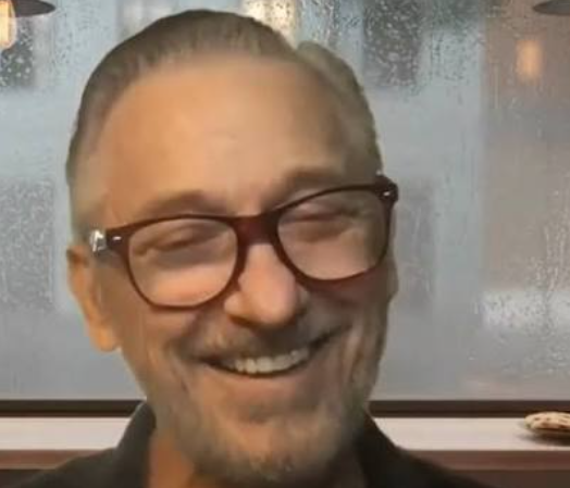 Smiling person with glasses in front of a soft-lit background
