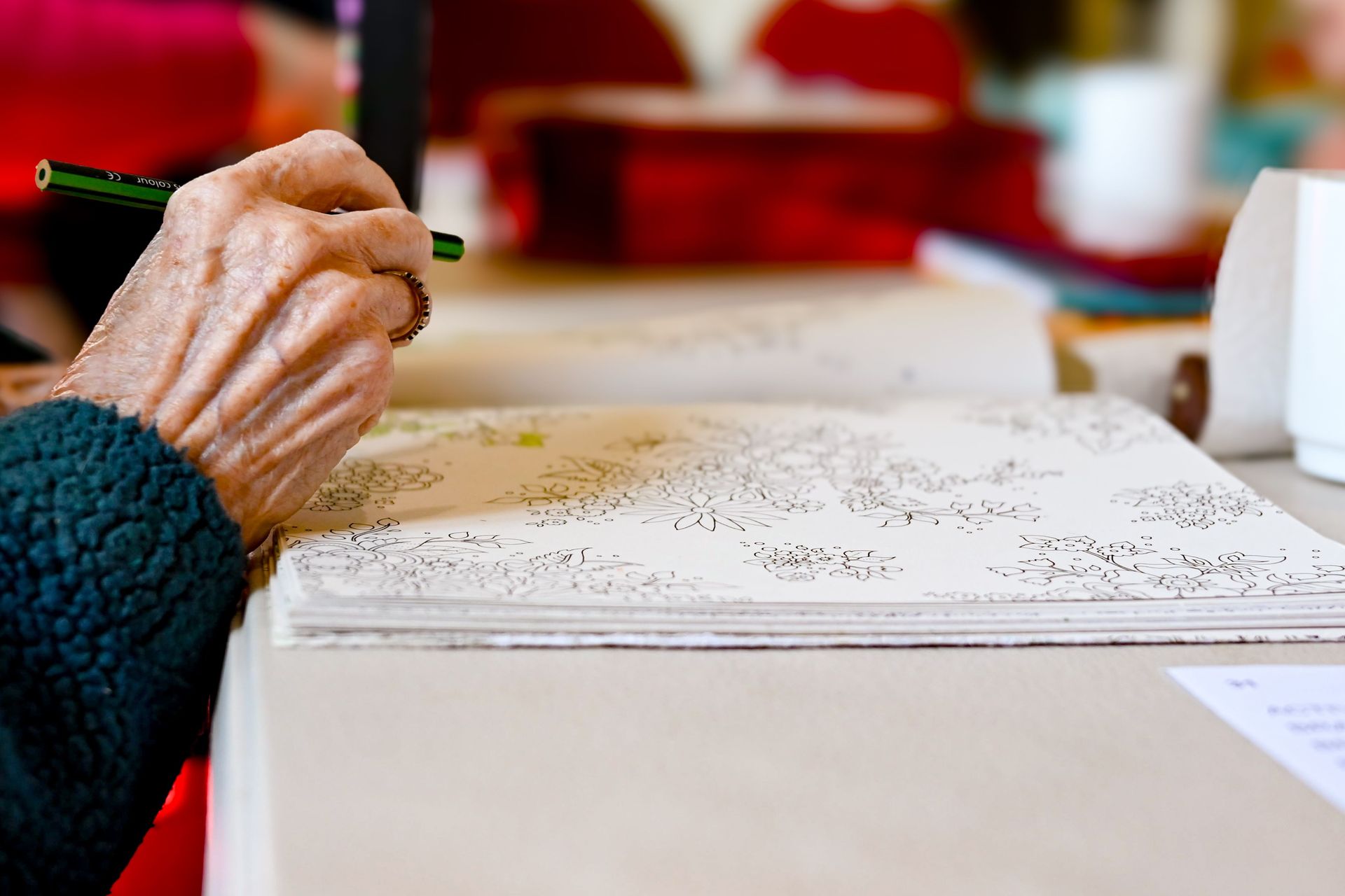 Hand writing with a green pencil on a large sheet of paper at a table
